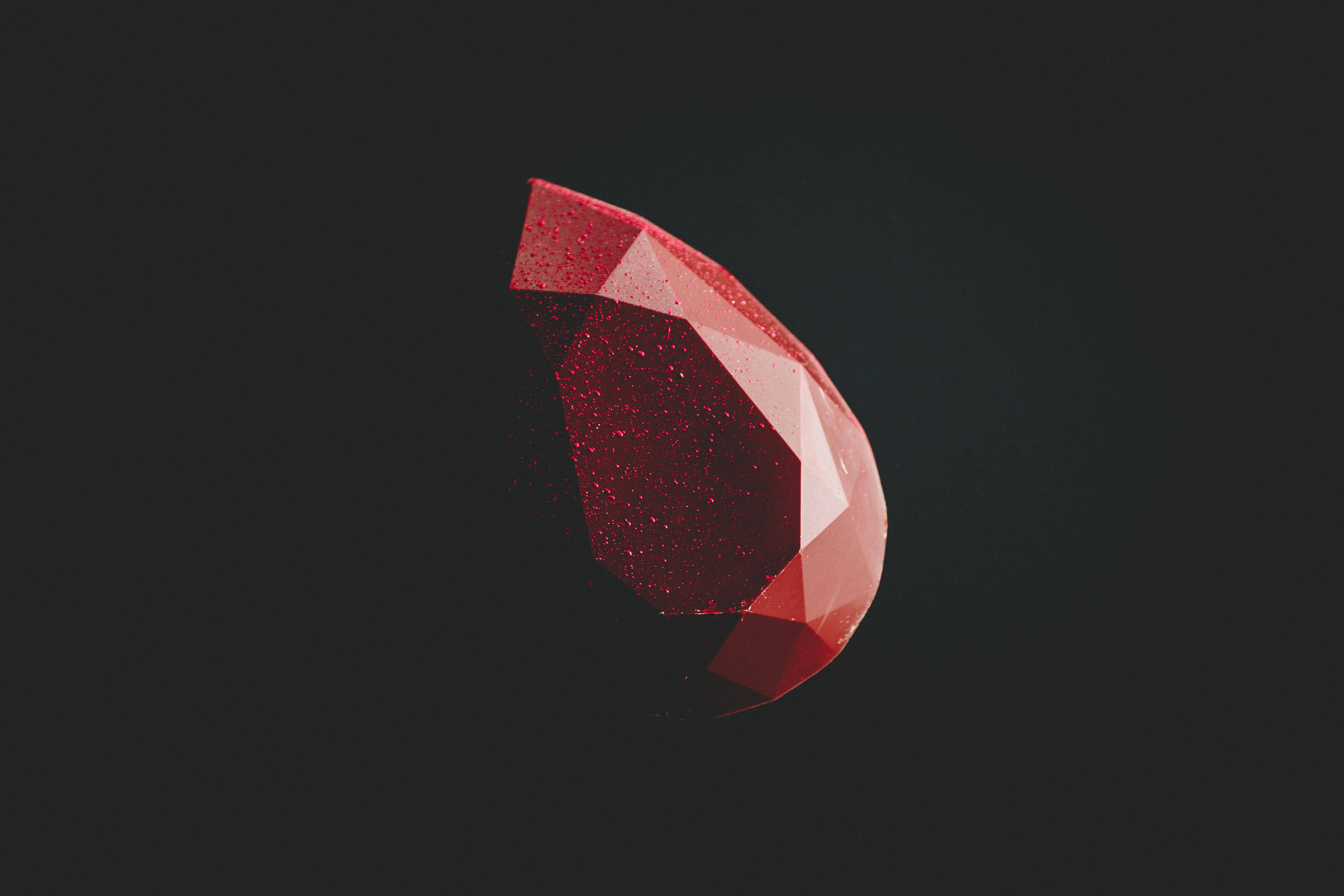 Dark Minimalist 桌布 壁紙 — 一顆切割面閃爍的紅色寶石漂浮在深色背景上。