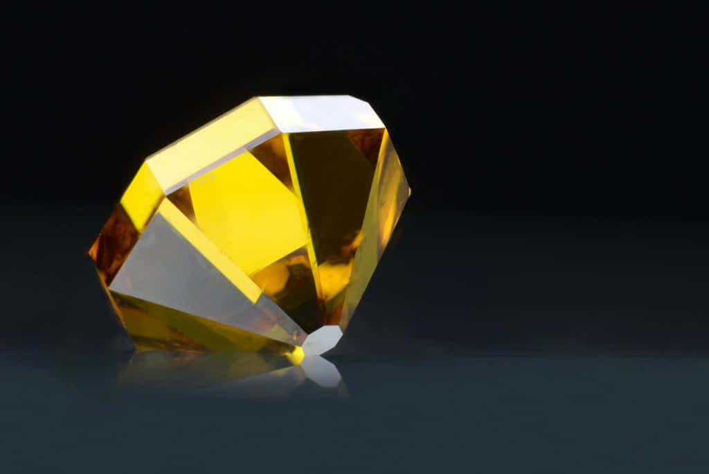 Yellow Diamond 桌布 壁紙 — 一顆切割面黃寶石在深色反光表面上閃耀著內部光芒。