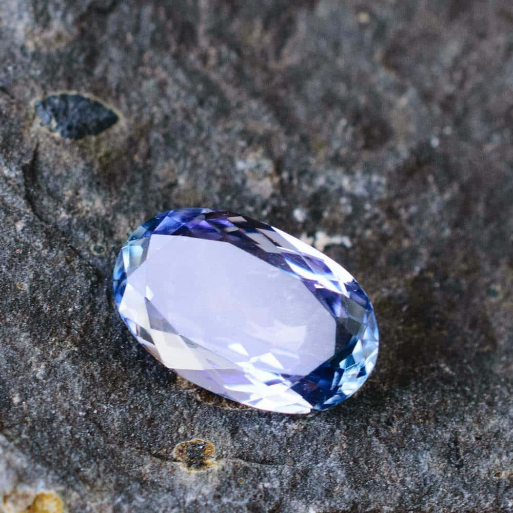 Crystal 桌布 壁紙 — 一顆刻面橢圓形藍寶石放在粗糙紋理的灰色岩石表面上。