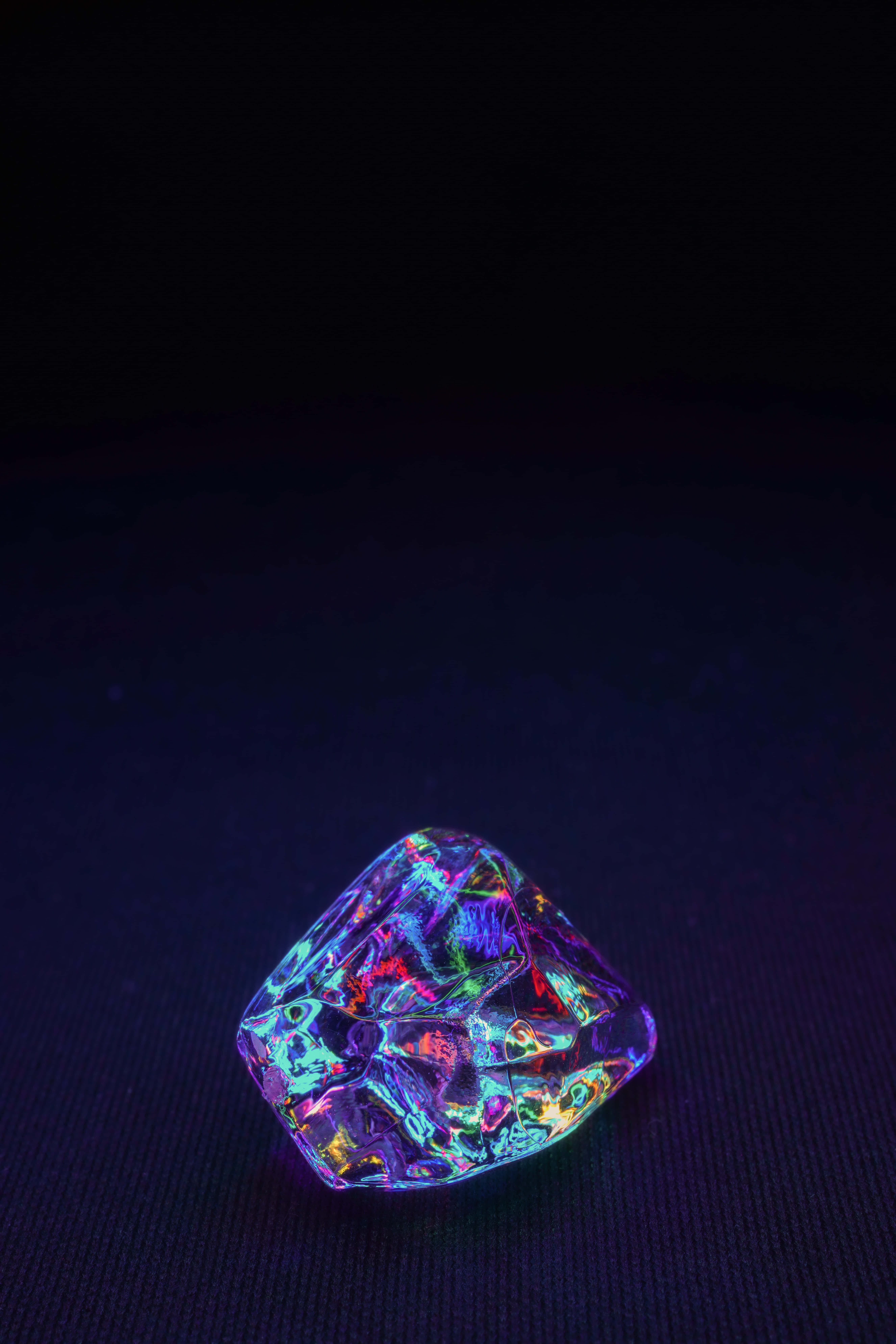 水晶 桌布 壁紙 — 一顆多面切割的水晶寶石在深黑色紋理背景上散發出鮮豔的彩虹色調。