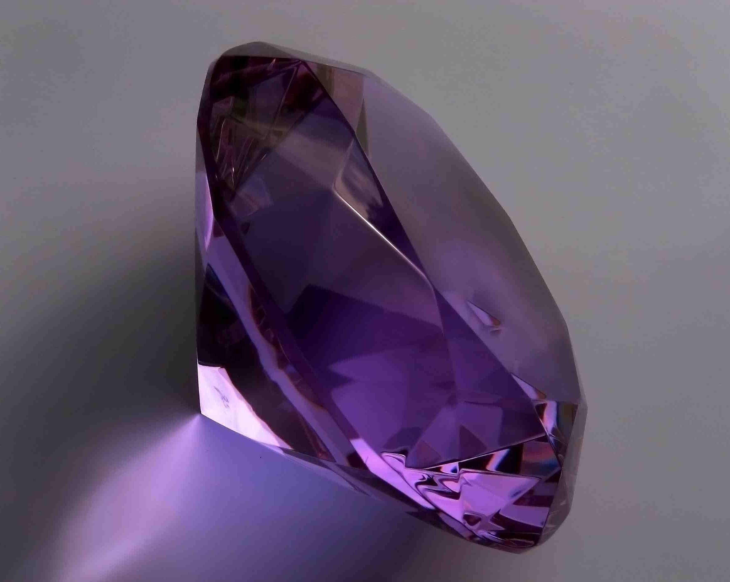紫水晶 桌布 壁紙 — 一顆大型切割紫色紫水晶寶石在柔和的灰色背景下閃耀著內部反射。