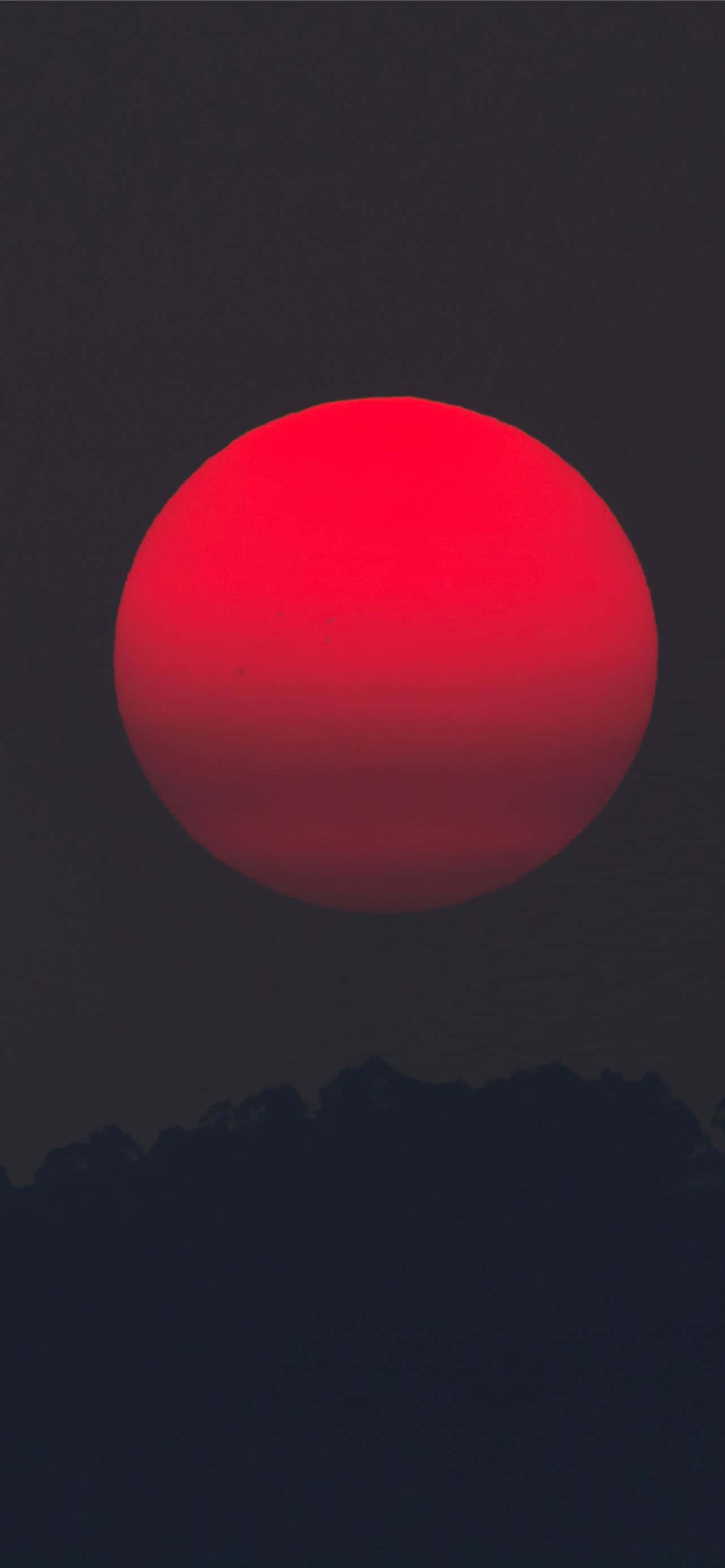 紅色 iPhone 桌布 壁紙 — 一顆巨大的熾熱紅太陽主宰著黃昏時分黑暗天空中輪廓分明的山峰。