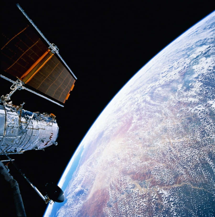 Hubble Space Telescope 桌布 壁紙 — 一顆帶有太陽能板的衛星環繞地球運行，展示了地球彎曲的地平線和旋轉的雲層，背景是漆黑的太空。