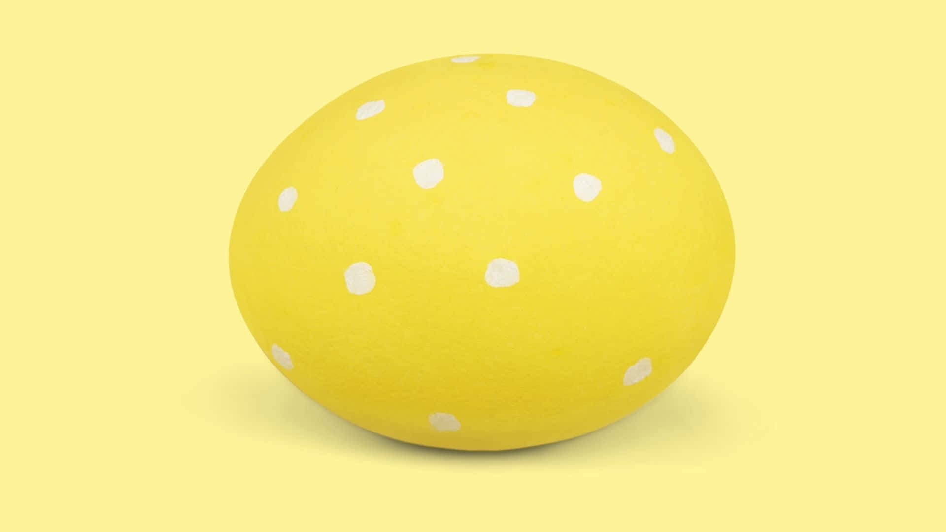 Easter Egg 桌布 壁紙 — 一顆帶有白色圓點的亮黃色雞蛋，居中放置在柔和的黃色背景上。