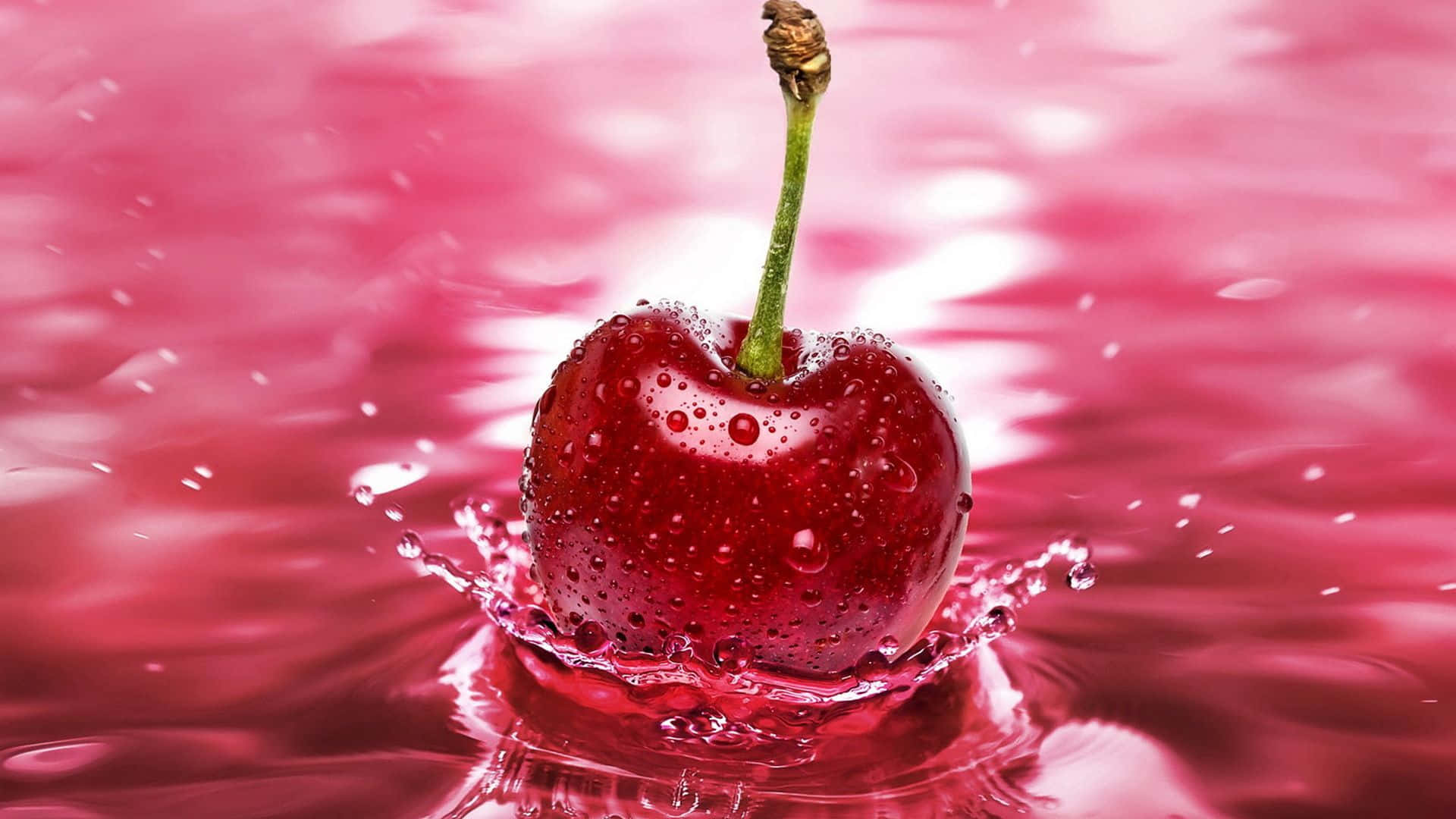 1920x1080 Red 桌布 壁紙 — 一顆帶有綠色莖的光澤紅櫻桃掉入粉紅色液體中，產生閃閃發光的水花。