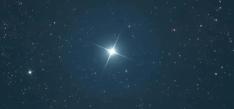 太空 桌布 壁紙 — 一顆帶有輻射尖刺的明亮恆星主導著深藍色星場，點綴著遠處閃爍的燈光。