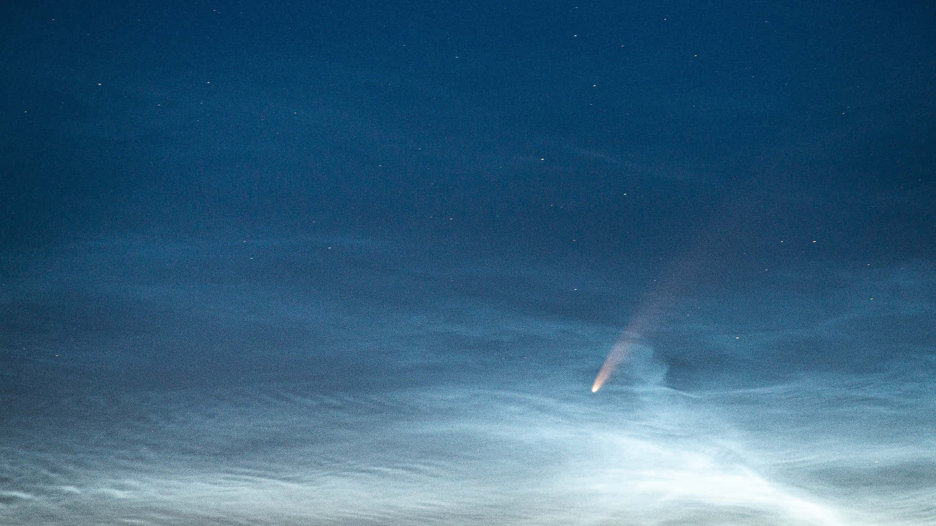 comet 桌布 壁紙 — 一顆彗星劃過繁星點點的夜空，下方有縷縷雲彩，在深藍色調中閃耀著明亮的光芒。