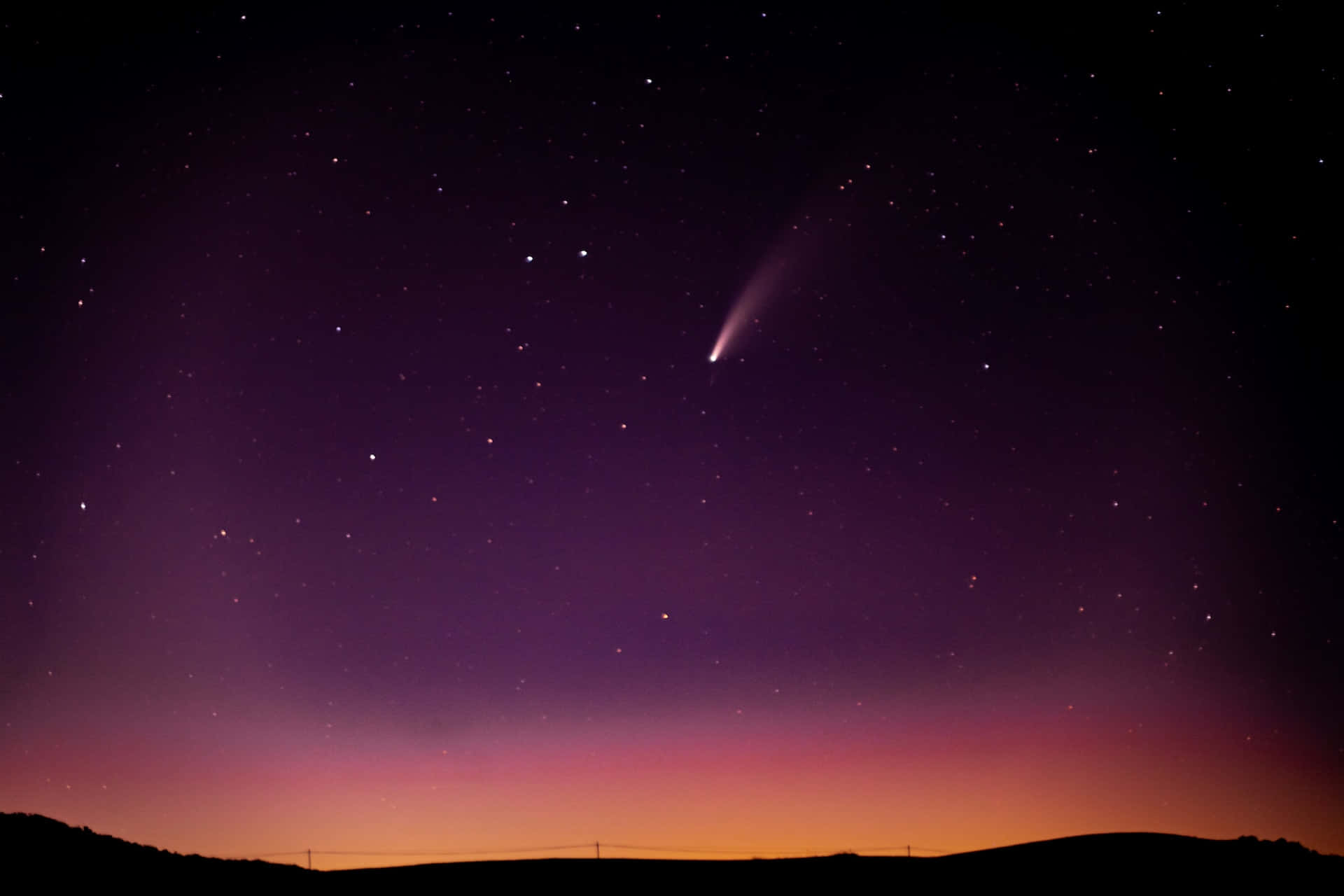 comet 桌布 壁紙 — 一顆彗星劃過繁星點點的暮色天空，下方是帶有紫色和橙色漸層的剪影山丘。