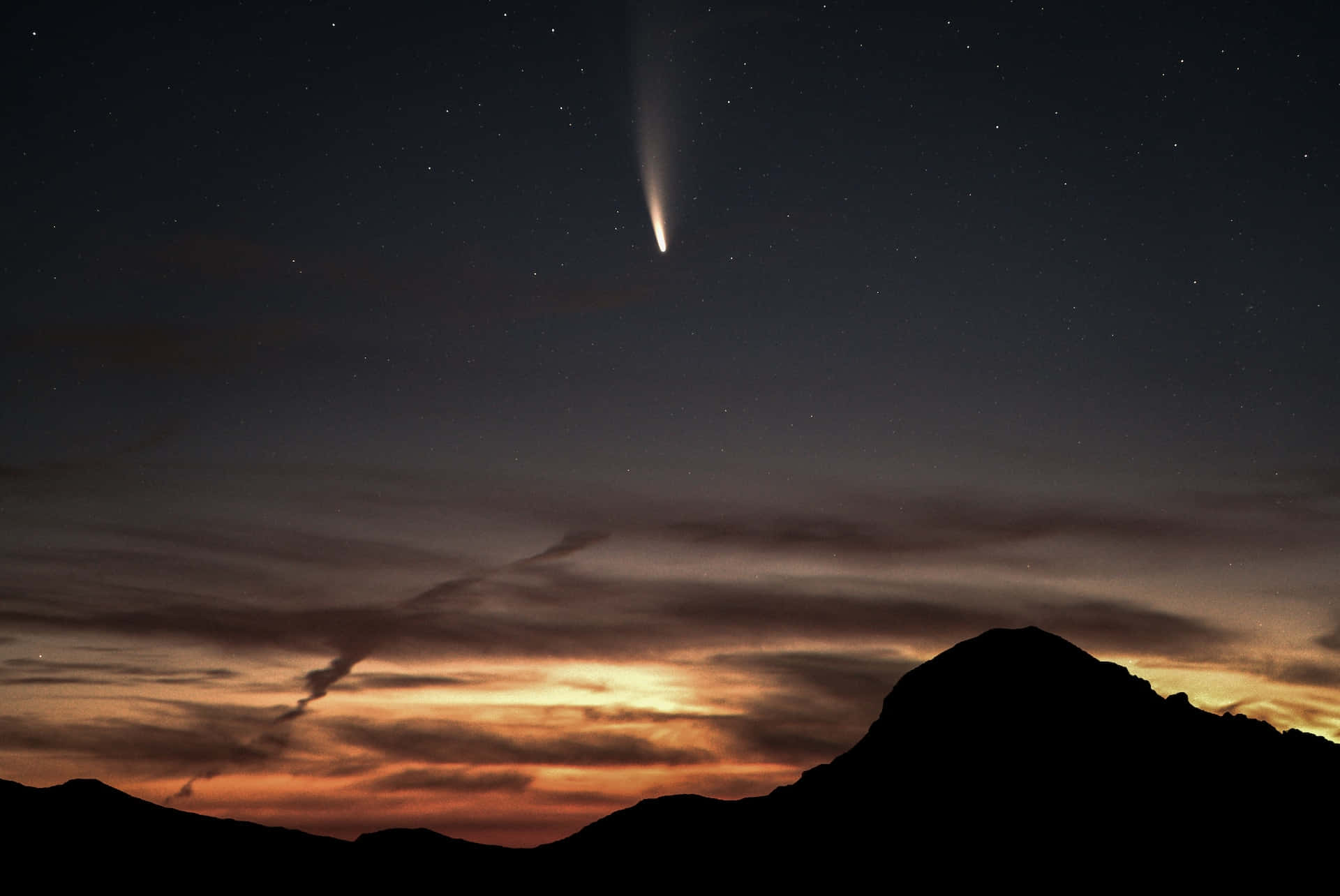 comet 桌布 壁紙 — 一顆明亮的彗星劃過繁星點點的暮色天空，下方是輪廓分明的山峰，閃爍著橙色和紫色的光芒。