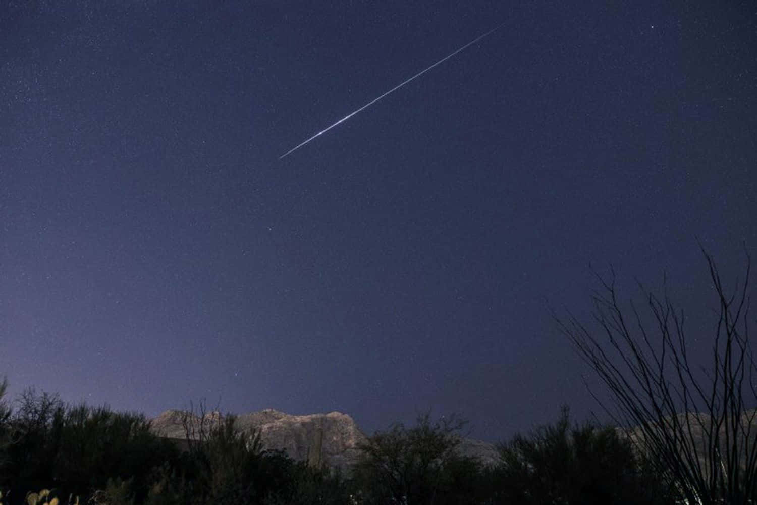 meteor 桌布 壁紙 — 一顆明亮的流星劃過星空夜空，下方是剪影般的沙漠山脈和稀疏的植被。