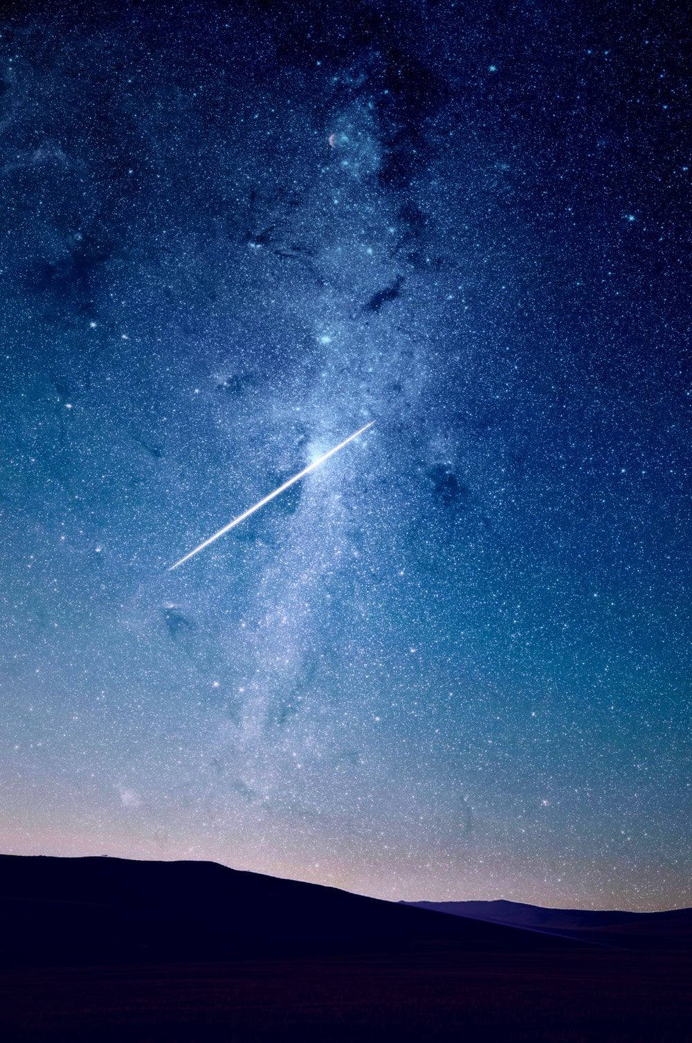 安卓 桌布 壁紙 — 一顆明亮的流星劃過繁星點點的夜空，下方是深藍色銀河下的黑暗起伏山丘。