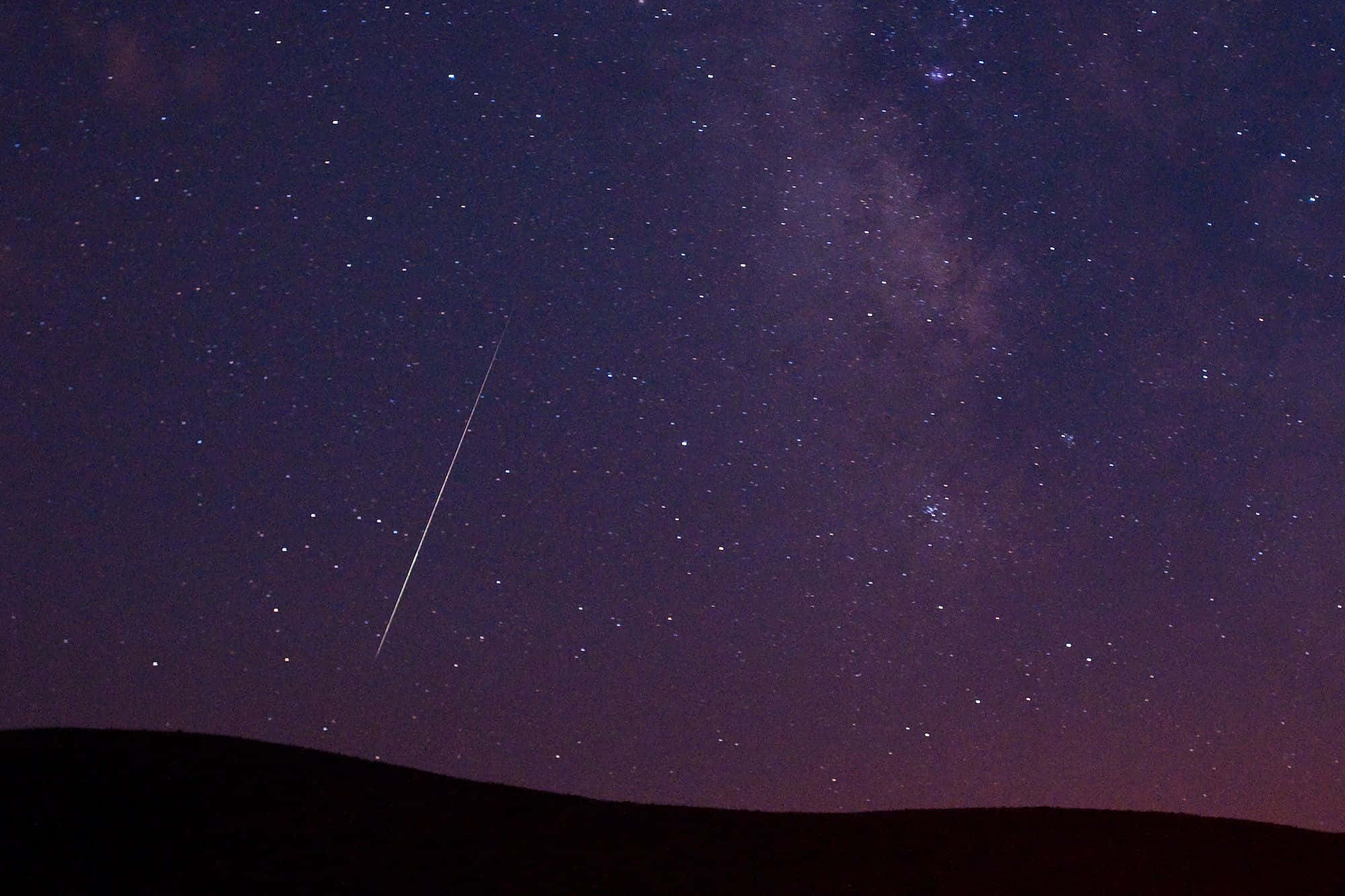 meteor 桌布 壁紙 — 一顆明亮的流星在銀河下劃過黑暗剪影山丘上方的星空。