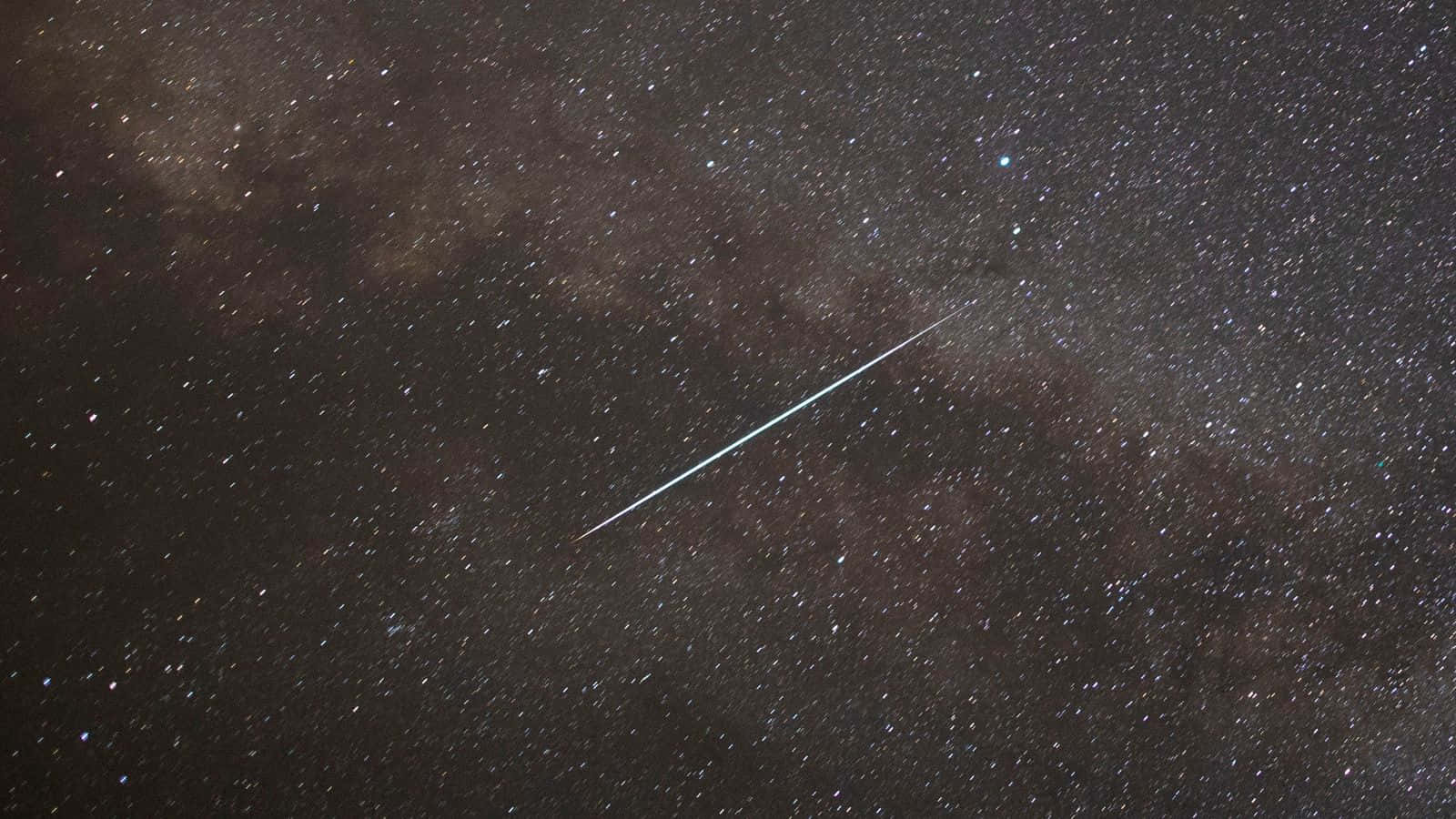 meteor 桌布 壁紙 — 一顆明亮的流星斜斜劃過密集的星場，其中有黑暗的宇宙雲和散落的星星。