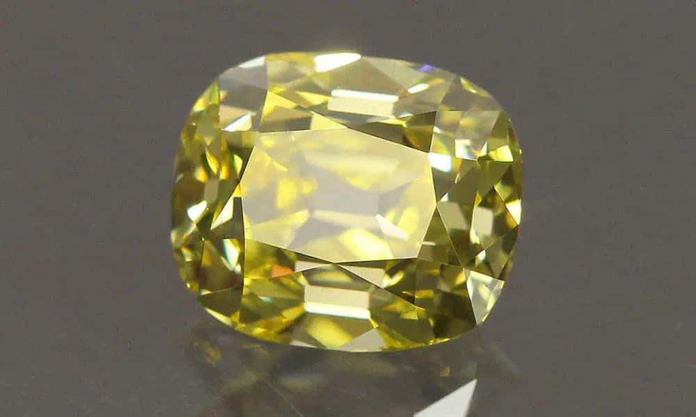 Yellow Diamond 桌布 壁紙 — 一顆明亮的黃色枕形切割寶石，在深色反光表面上閃耀著精確的刻面。