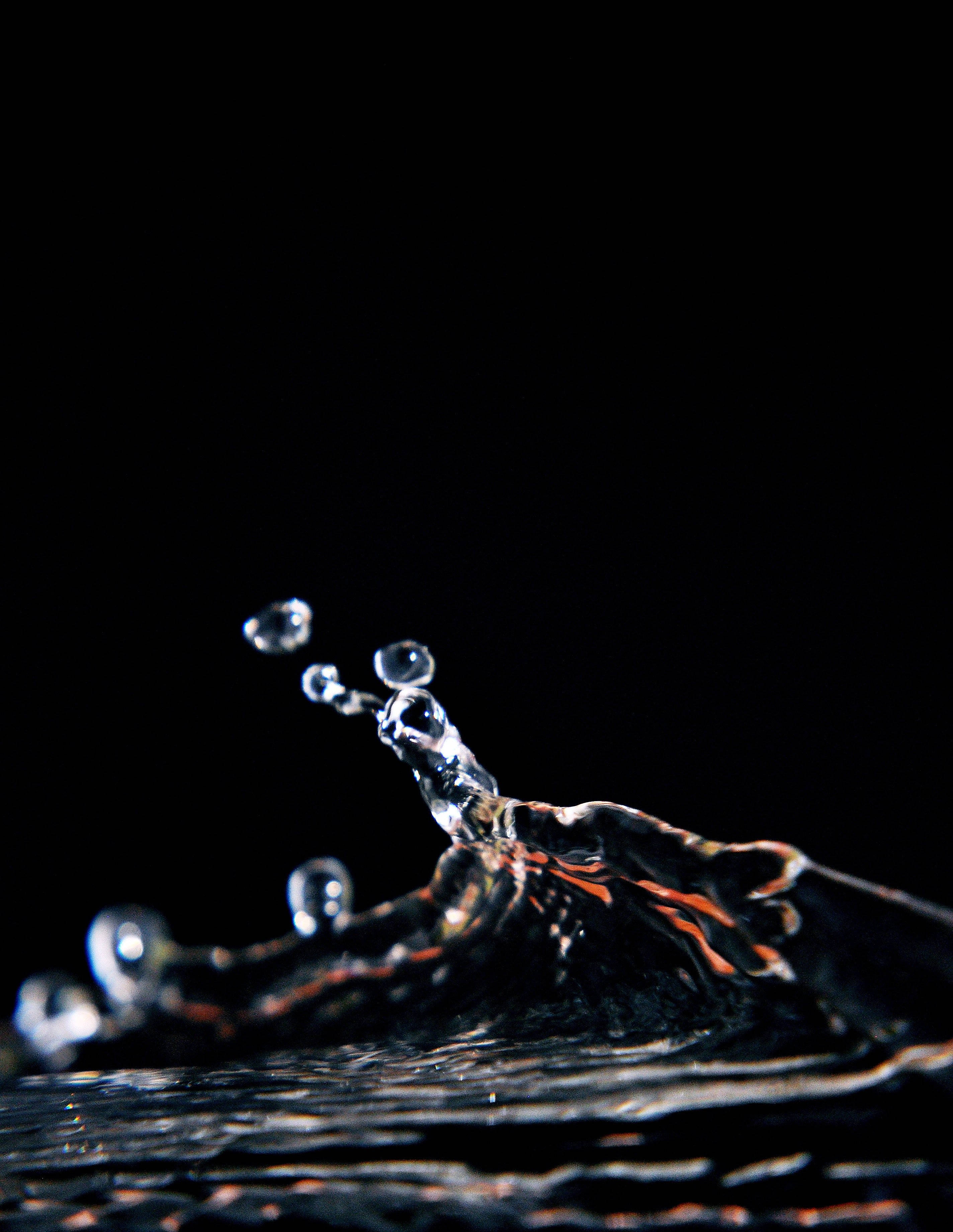 水 桌布 壁紙 — 一顆晶瑩剔透的水滴在純黑背景上定格於半空中，帶有發光的橙色反射。