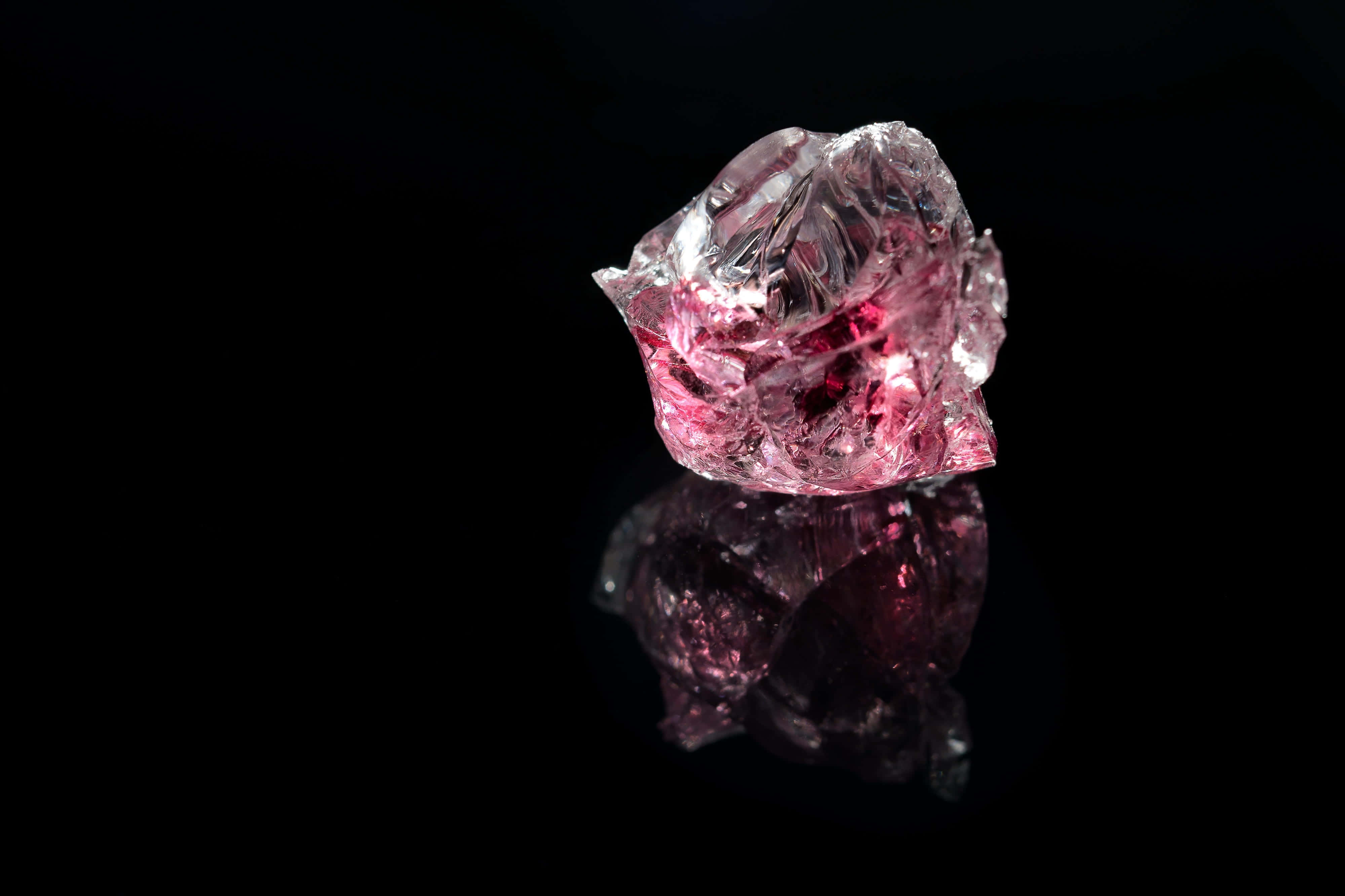 Pink Crystal Quartz 桌布 壁紙 — 一顆未經加工的粉紅鑽石在黑色反光表面上閃耀著內部的火焰。