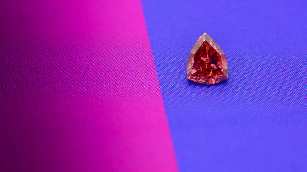 Red Diamond 桌布 壁紙 — 一顆梨形紅色寶石在充滿活力的洋紅色和電光藍色布料背景上閃耀著火彩般的刻面。