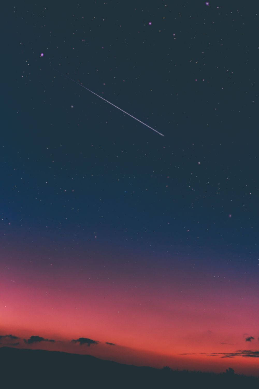 夜空 桌布 壁紙 — 一顆流星劃過暮色天空，從深藍色過渡到火熱的粉紅色，映襯著山丘的剪影。