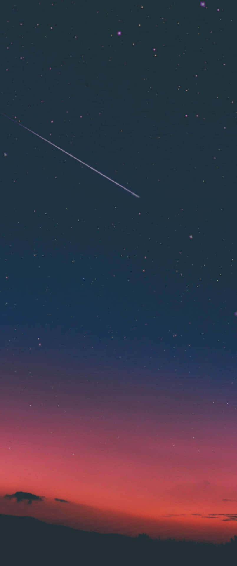 直式 桌布 壁紙 — 一顆流星劃過暮色天空，從深藍色過渡到火橙色，背景是輪廓分明的山丘。