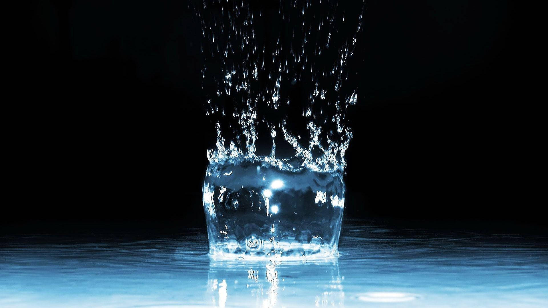 Water Splash 桌布 壁紙 — 一顆清澈如水晶的水滴在黑色背景上以慢動作向上飛濺，帶有發光的藍色反射。