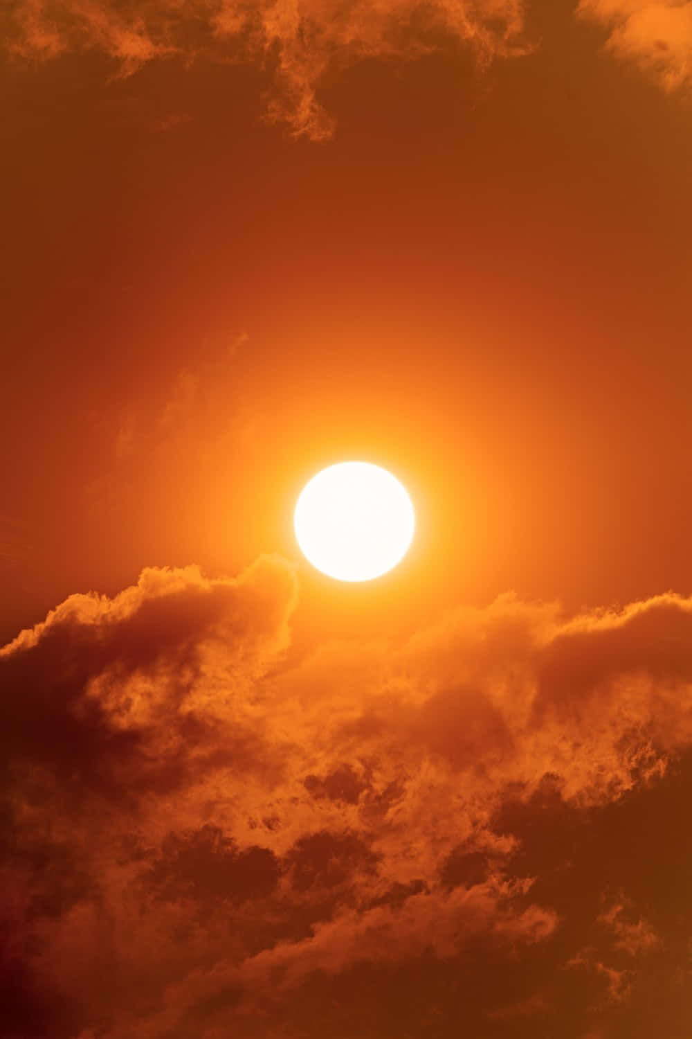 雲朵 桌布 壁紙 — 一顆燦爛的太陽在熾熱的橙色雲層中強烈發光，構成戲劇性的日落天空。