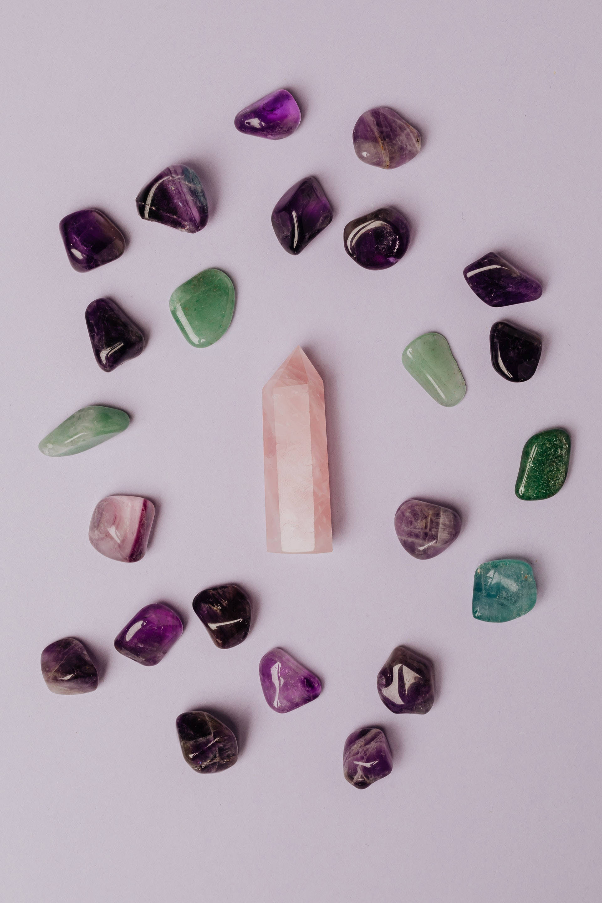 紫水晶 桌布 壁紙 — 一顆玫瑰石英水晶在柔和的薰衣草背景上，中心位置站立於散落的紫水晶和綠色東陵石之間。