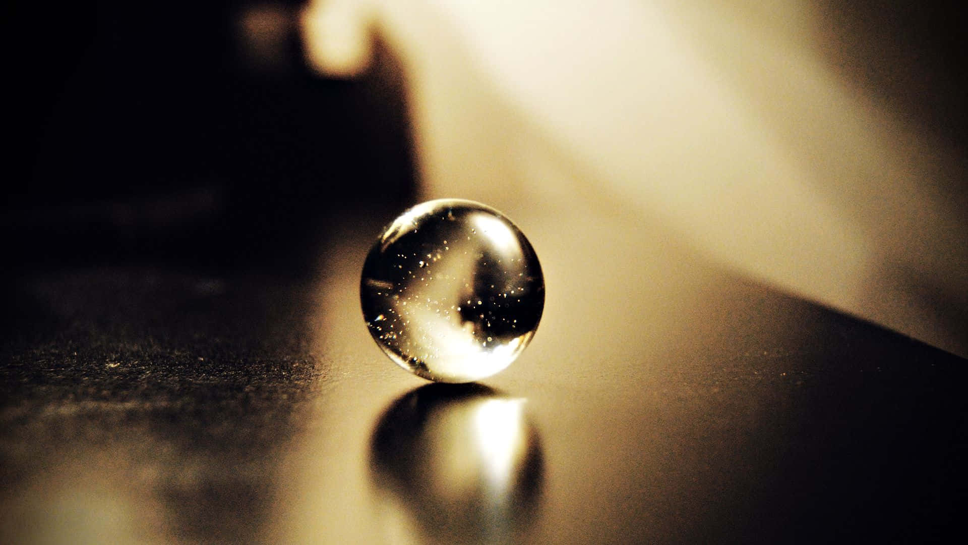 Crystal Ball 桌布 壁紙 — 一顆玻璃彈珠放在深色表面上，反射出溫暖的金色光芒，背景柔和散景。