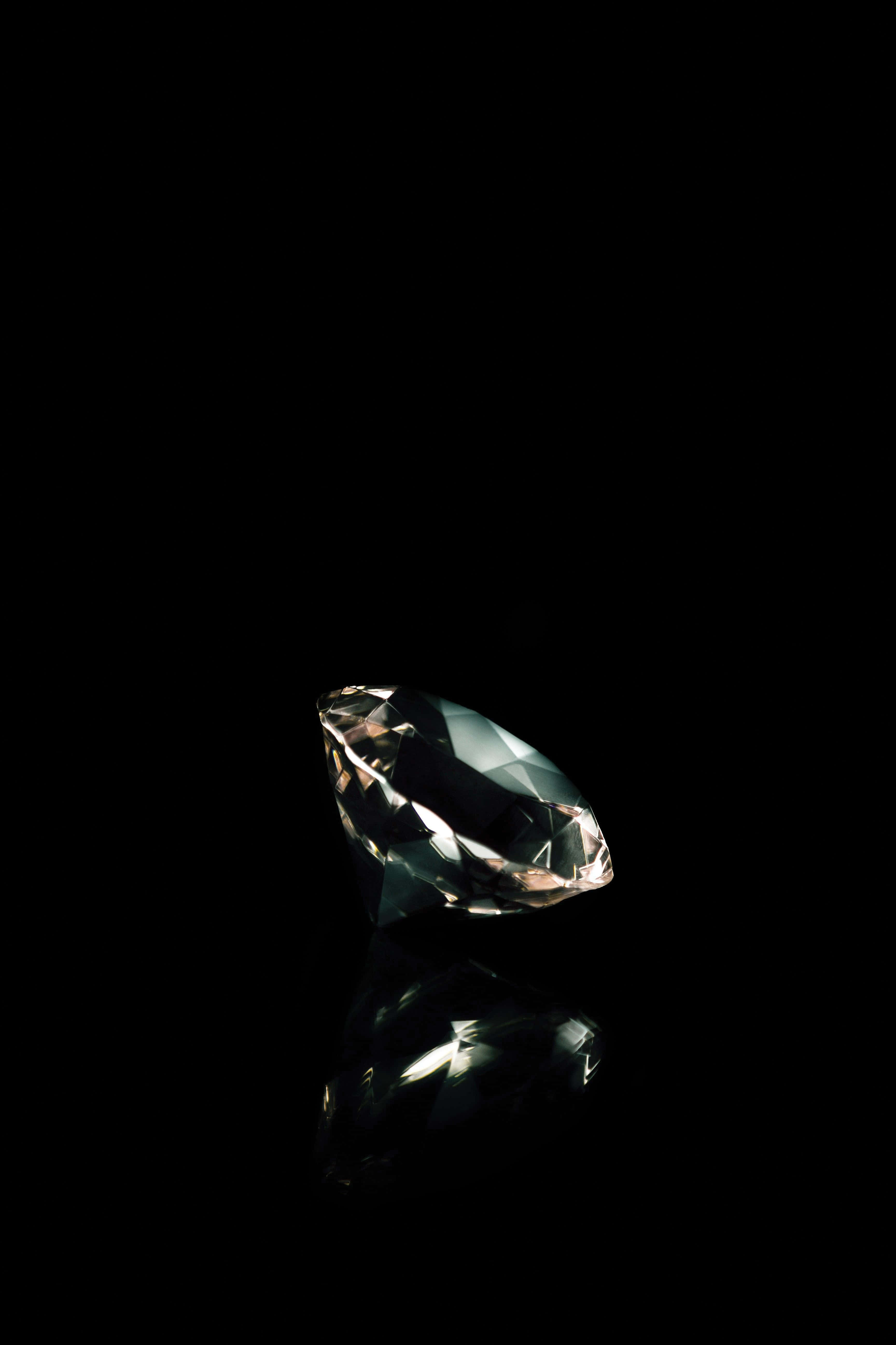 diamonds 桌布 壁紙 — 一顆璀璨的鑽石在純黑背景上閃耀著鋒利的切面，下方投射出鏡面般的倒影。