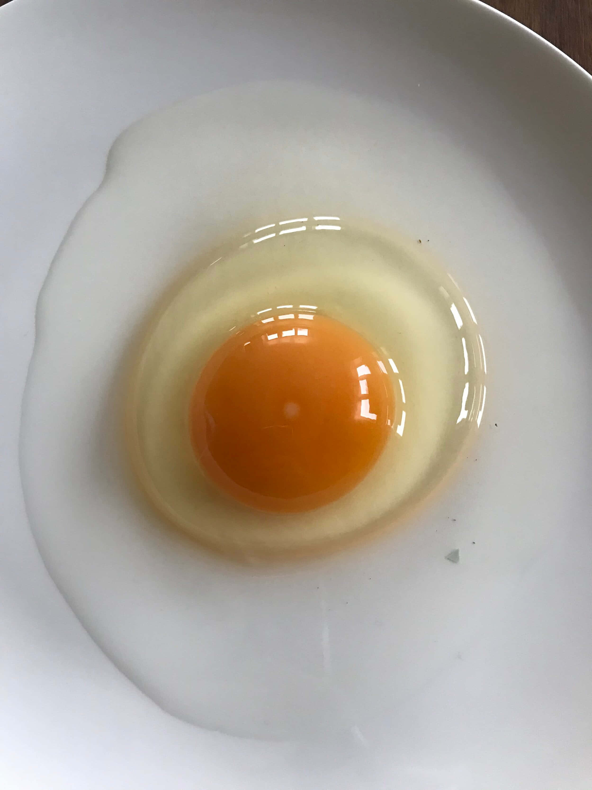 Egg 桌布 壁紙 — 一顆生雞蛋，帶有鮮豔的橙色蛋黃和清澈的蛋白，置於純白色盤子中央。