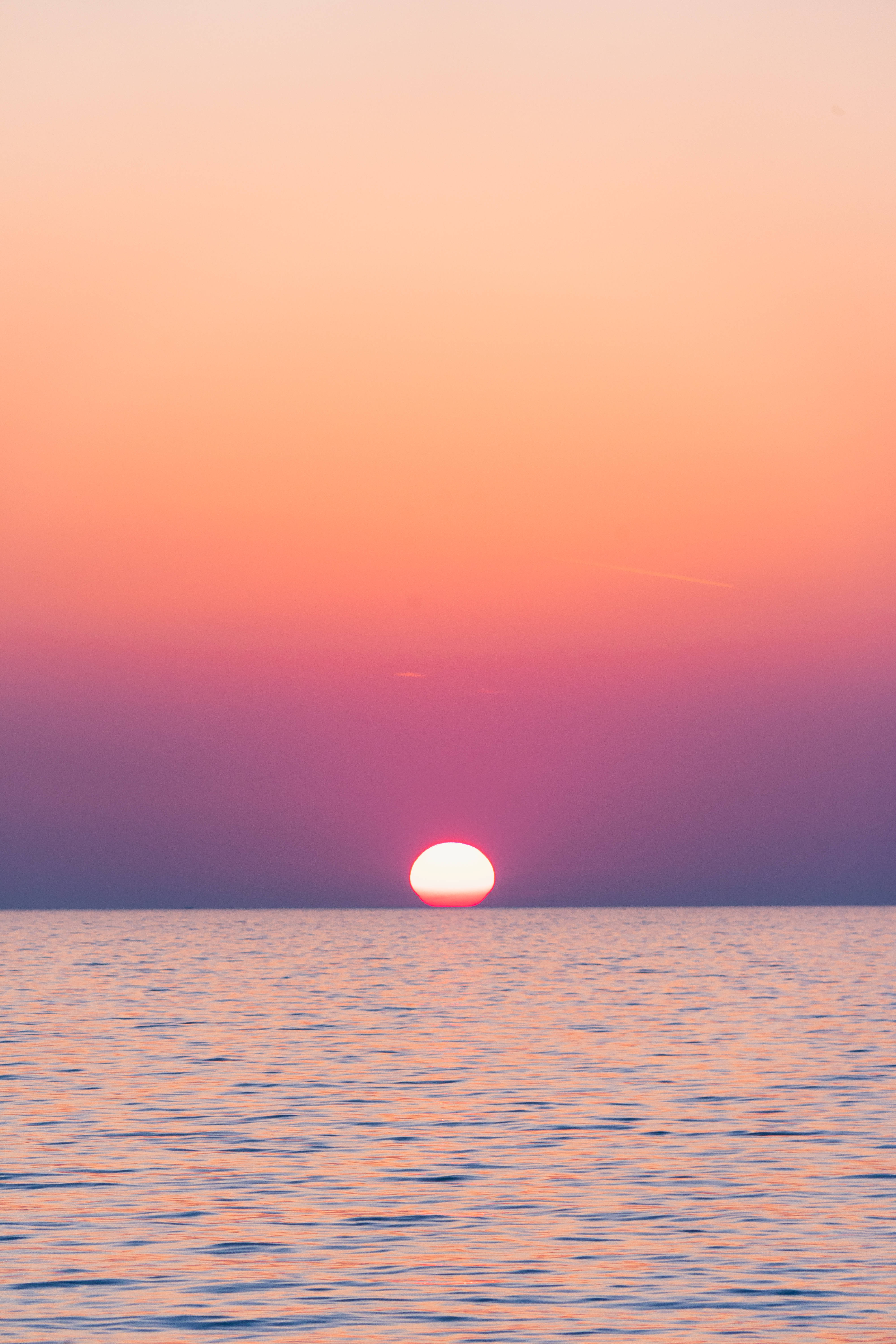 Aesthetic Sky 桌布 壁紙 — 一顆發光的太陽沉入地平線以下，在平靜的海面上投射出充滿活力的粉紅色和橙色色調。