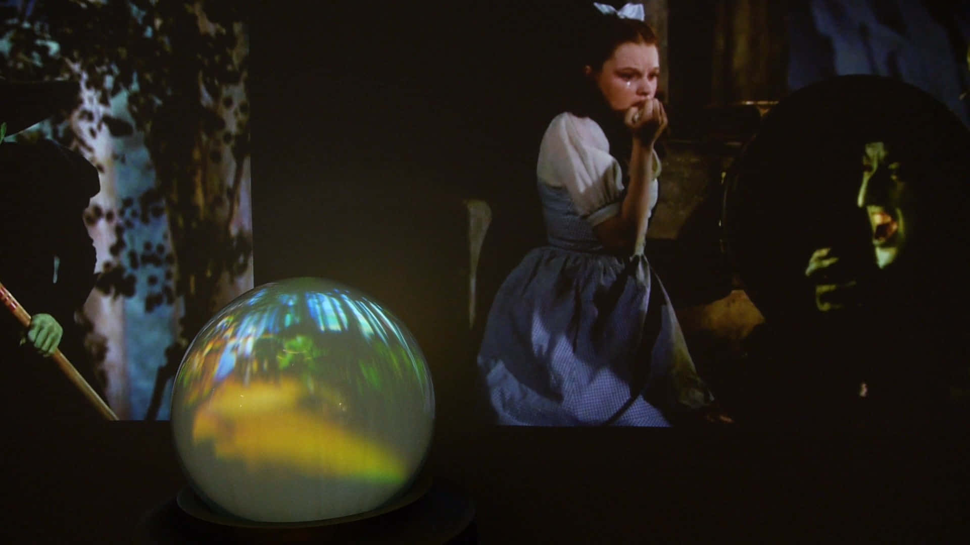 Crystal Ball 桌布 壁紙 — 一顆發光的水晶球反射出五彩繽紛的光芒，同時投射在黑暗房間周圍牆壁上的女孩和女巫的電影場景正在播放。
