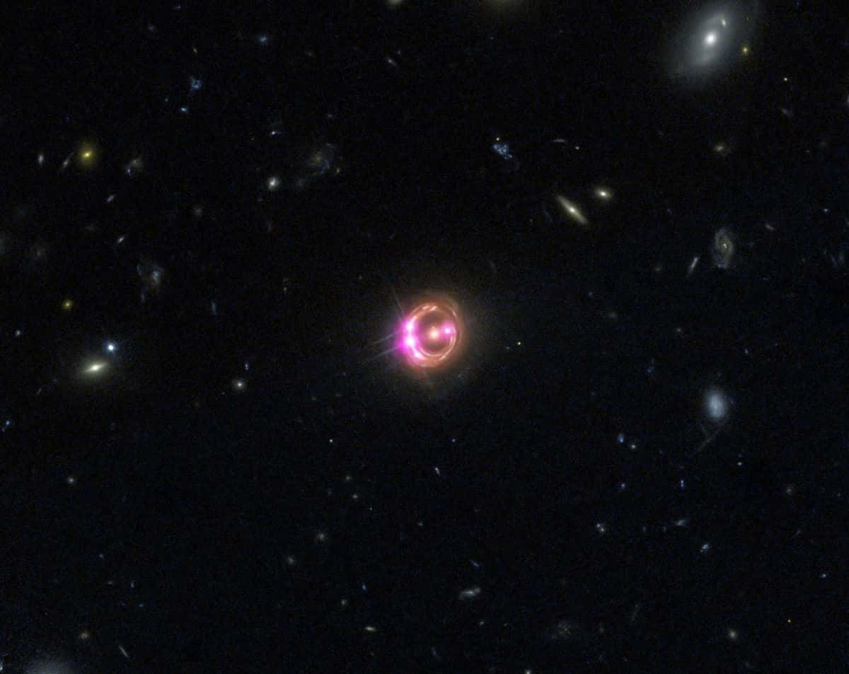Quasar 桌布 壁紙 — 一顆發光的粉紅色環狀類星體在深空中，以遙遠星系和恆星為背景，明亮地閃耀。