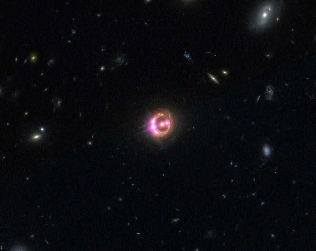 Quasar 桌布 壁紙 — 一顆發光的粉紅色環狀類星體在深空中，以遙遠星系和恆星為背景，明亮地閃耀。