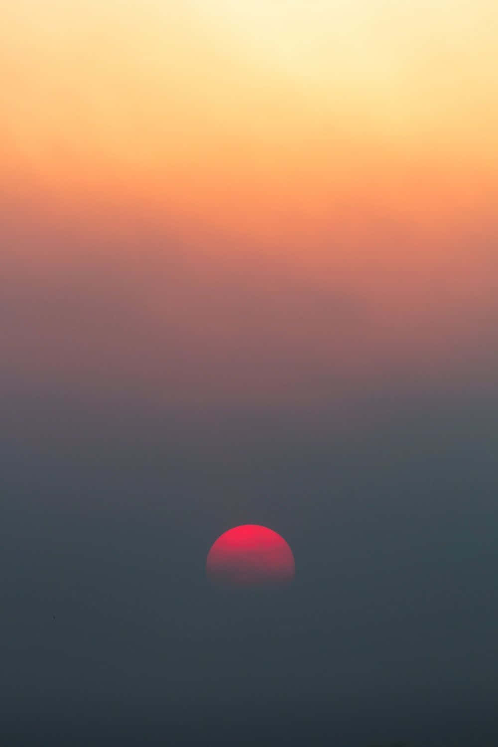 Dark Gradient 桌布 壁紙 — 一顆發光的紅色太陽沉入朦朧的地平線下，將天空染成溫暖的橙色和柔和的紫色漸變。