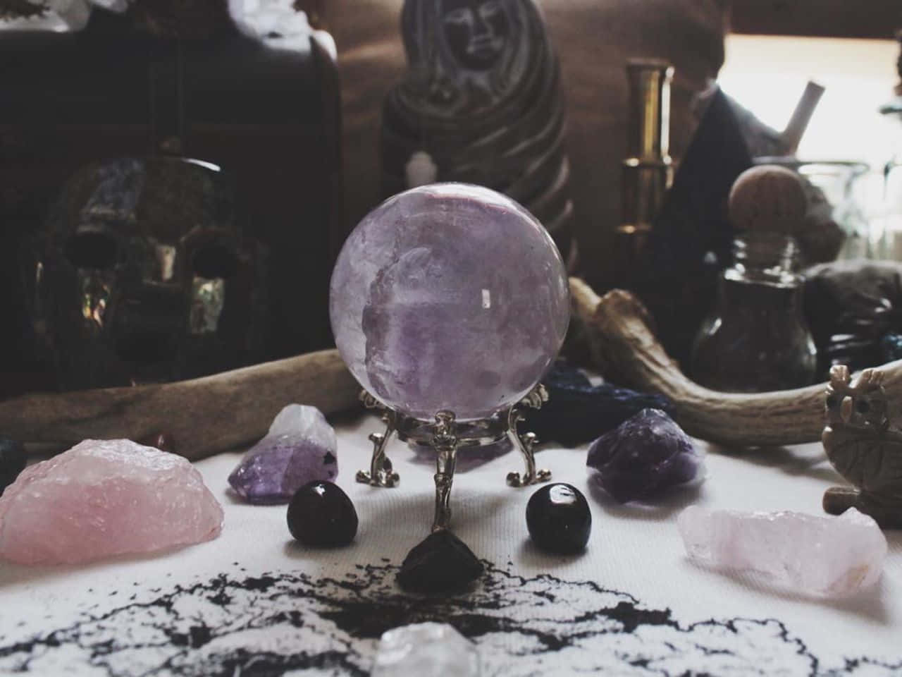 Crystal Ball 桌布 壁紙 — 一顆發光的紫色水晶球放置在一個華麗的支架上，周圍環繞著未經加工的寶石和神秘物品，處於一個燈光昏暗的神聖空間中。