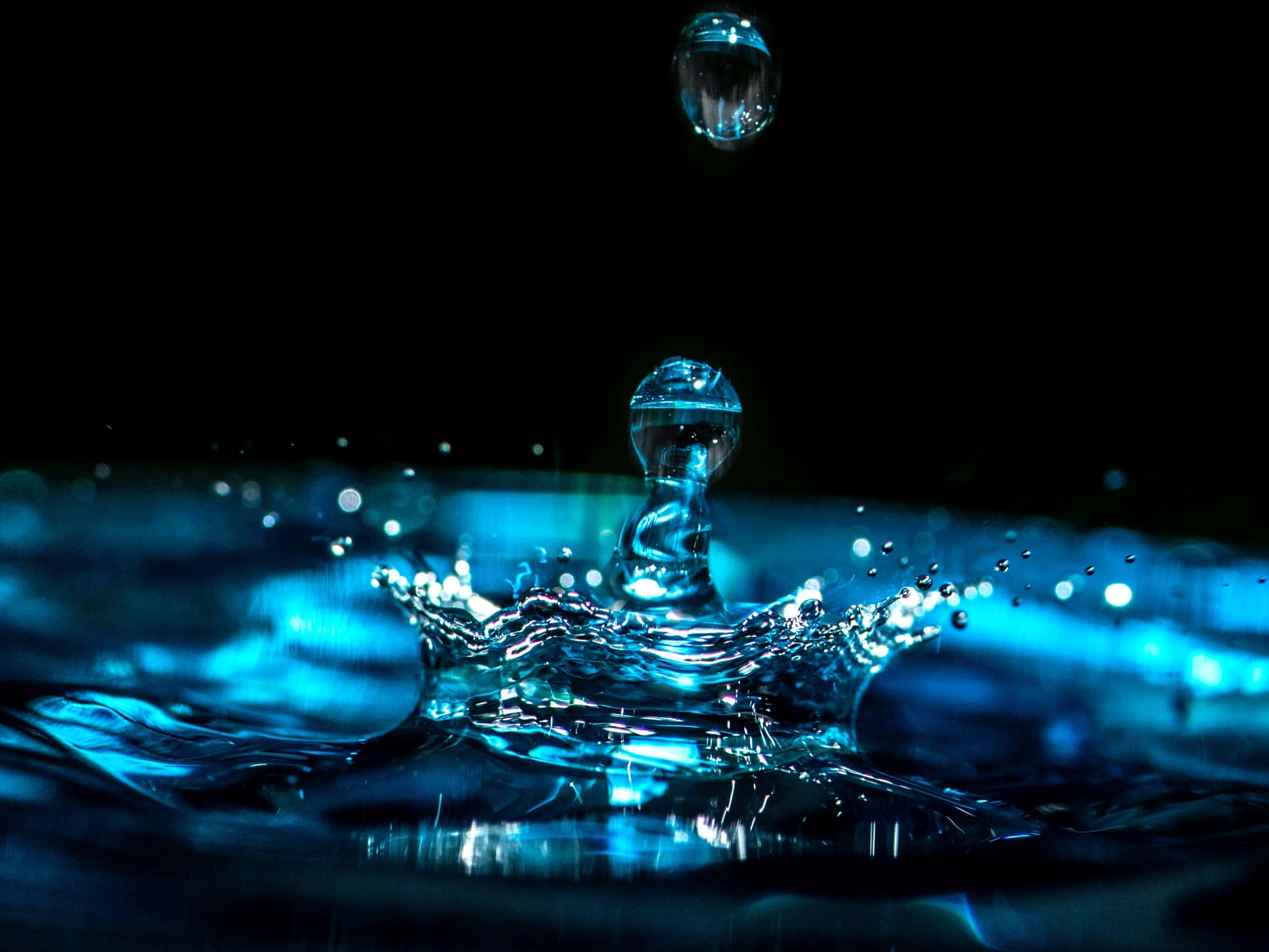 Hydration 桌布 壁紙 — 一顆發光的藍色水滴懸浮在漣漪表面上方，在黑色背景上形成皇冠狀的水花。