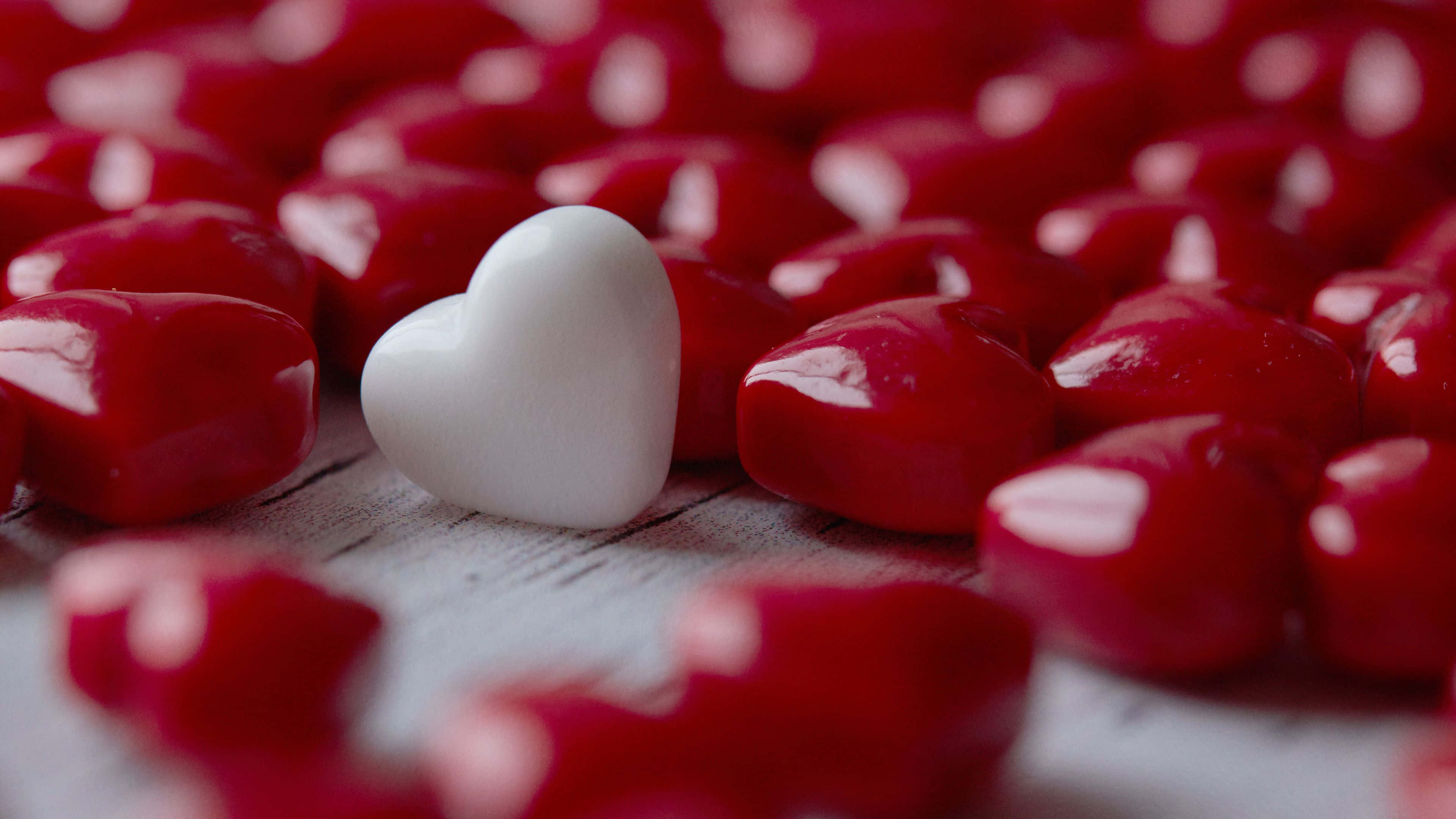 Sweet Love 桌布 壁紙 — 一顆白色心形糖果在一片閃亮紅色心形糖果中脫穎而出，置於經風化的木質表面上。