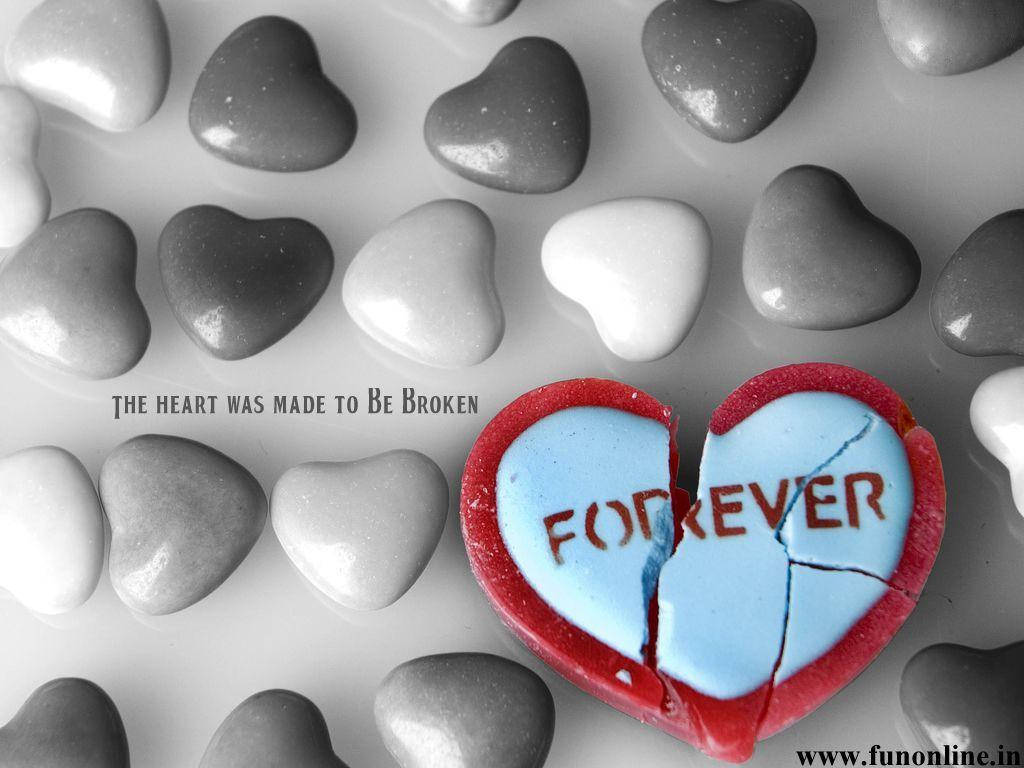 愛心 桌布 壁紙 — 一顆破碎的紅色心形糖果，上面寫著「FOREVER」分成兩半，放在灰階心形石頭之間。