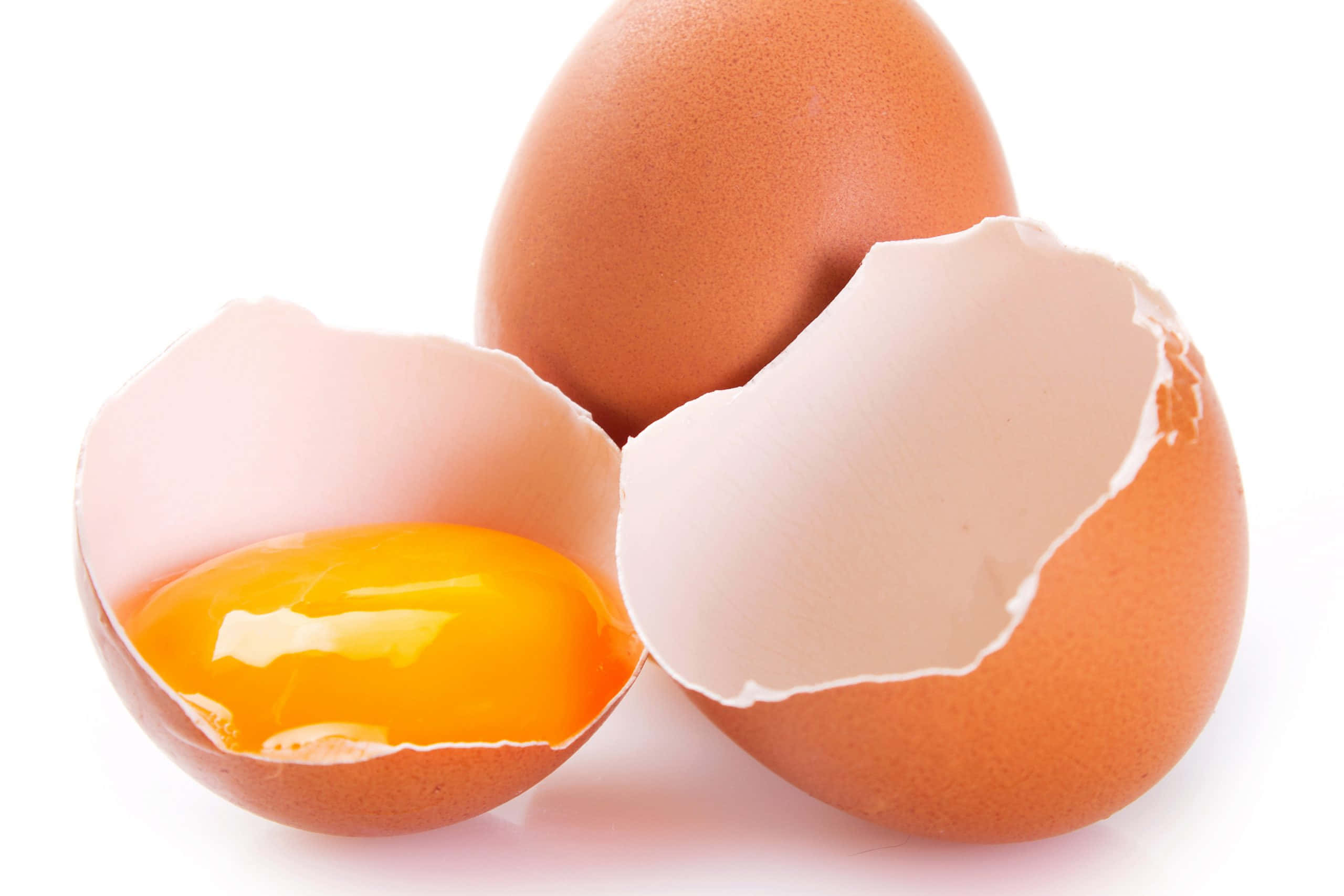 Eggshell 桌布 壁紙 — 一顆破裂的棕色雞蛋在純白背景上露出鮮黃色的蛋黃，旁邊還有另一顆完整的雞蛋。