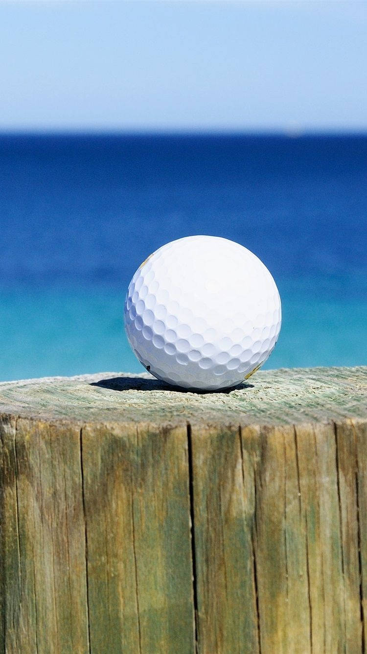 Golfing 桌布 壁紙 — 一顆純淨白色高爾夫球擱在風化的木柱上，背景是充滿活力的藍色海洋。