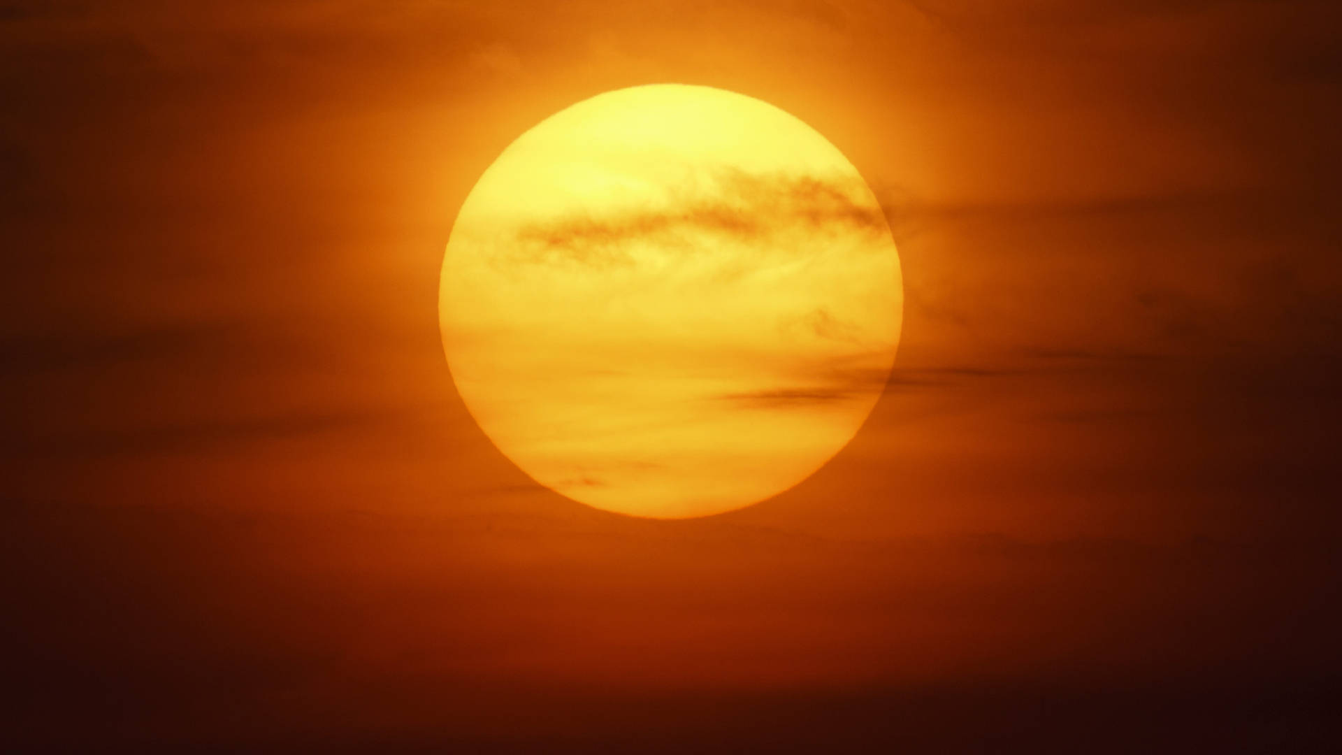Orange Circle 桌布 壁紙 — 一顆耀眼的橙色太陽主宰著天空，夕陽下縷縷雲彩飄過其發光的臉龐。
