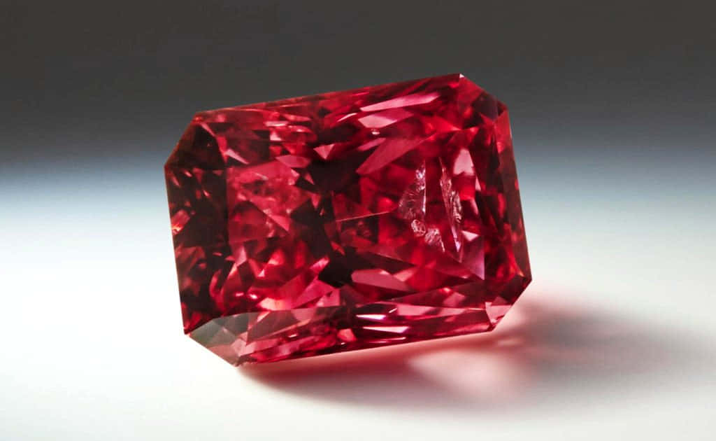 Red Diamond 桌布 壁紙 — 一顆閃耀的長方形紅色寶石，帶有複雜的切割面，在柔和的漸變背景上閃爍光芒。