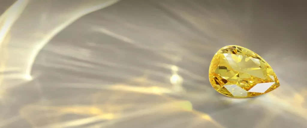 Yellow Diamond 桌布 壁紙 — 一顆閃耀的黃色梨形鑽石，在帶有光線條紋的柔和金色抽象背景上閃爍。