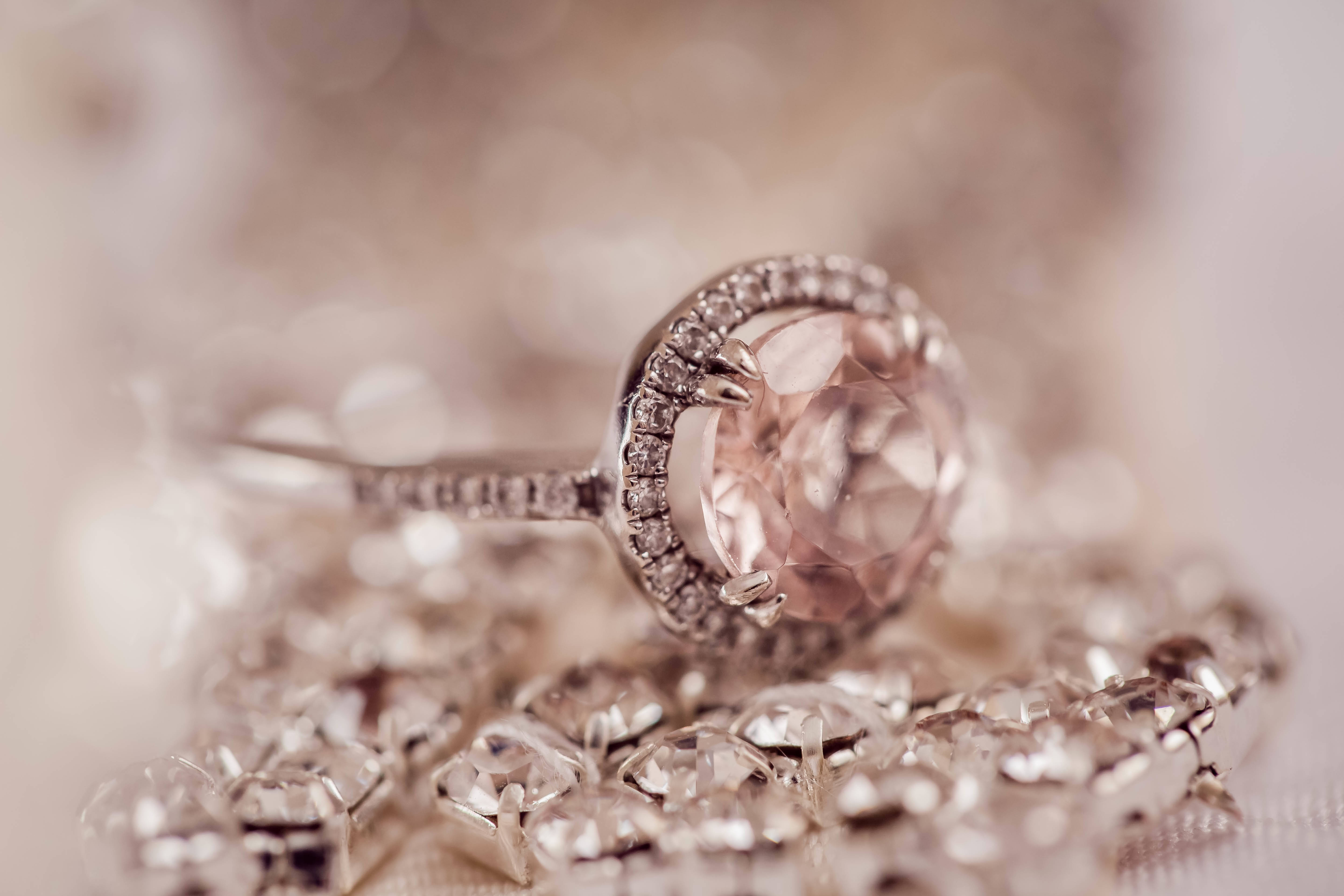 the ring 桌布 壁紙 — 一顆閃閃發光的玫瑰金戒指，鑲有大型粉紅色寶石，周圍環繞鑽石，置於散落的水晶床上。