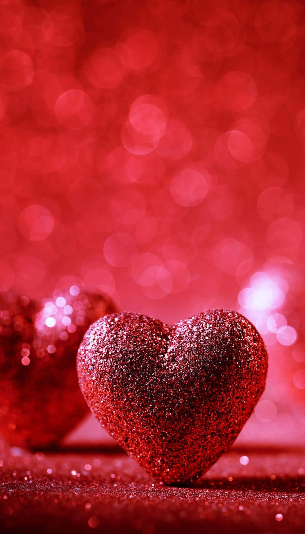 Red Cute Aesthetic 桌布 壁紙 — 一顆閃閃發光的紅色心形放在閃爍的表面上，背景是夢幻的紅色散景。