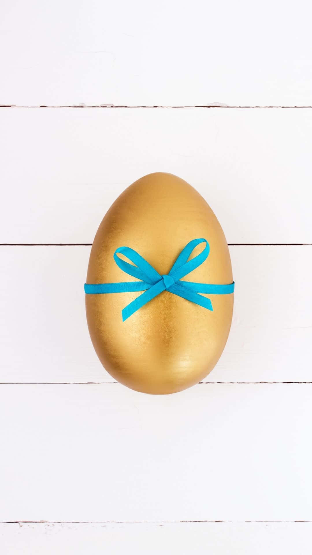 Easter Egg 桌布 壁紙 — 一顆閃閃發光的金蛋，飾有亮藍色絲帶，置於白色木板的中央。