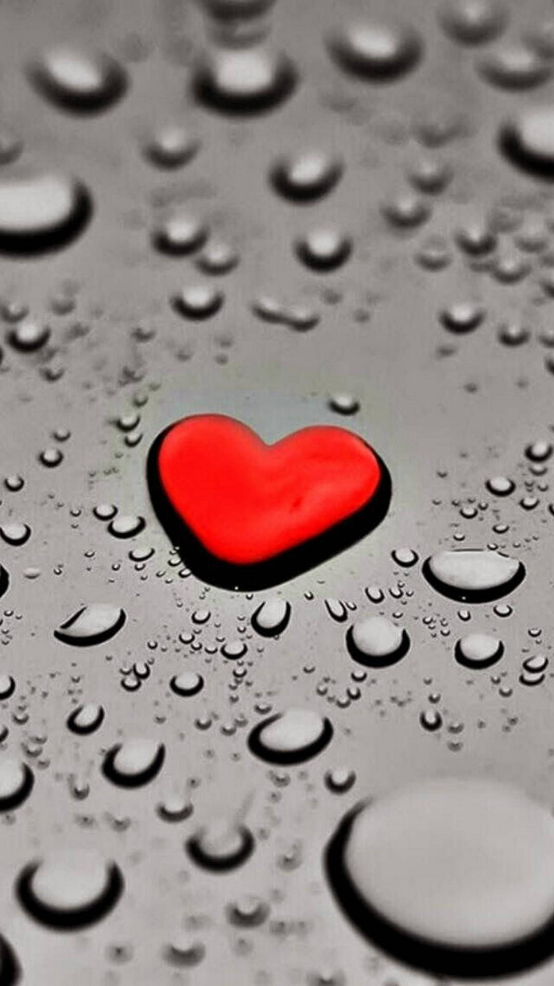 Love iPhone 桌布 壁紙 — 一顆鮮紅色的心臟放在銀色表面上，表面點綴著閃閃發光的水滴。