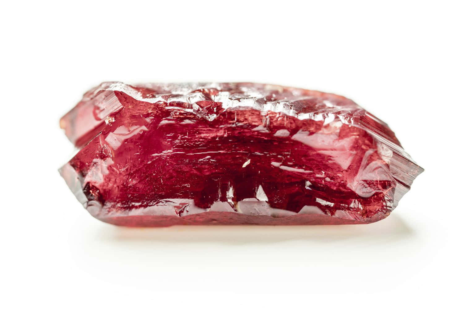 Ruby 桌布 壁紙 — 一顆鮮紅色的水晶，帶有鋸齒狀的刻面和內部裂縫，在純白色背景上閃閃發光。