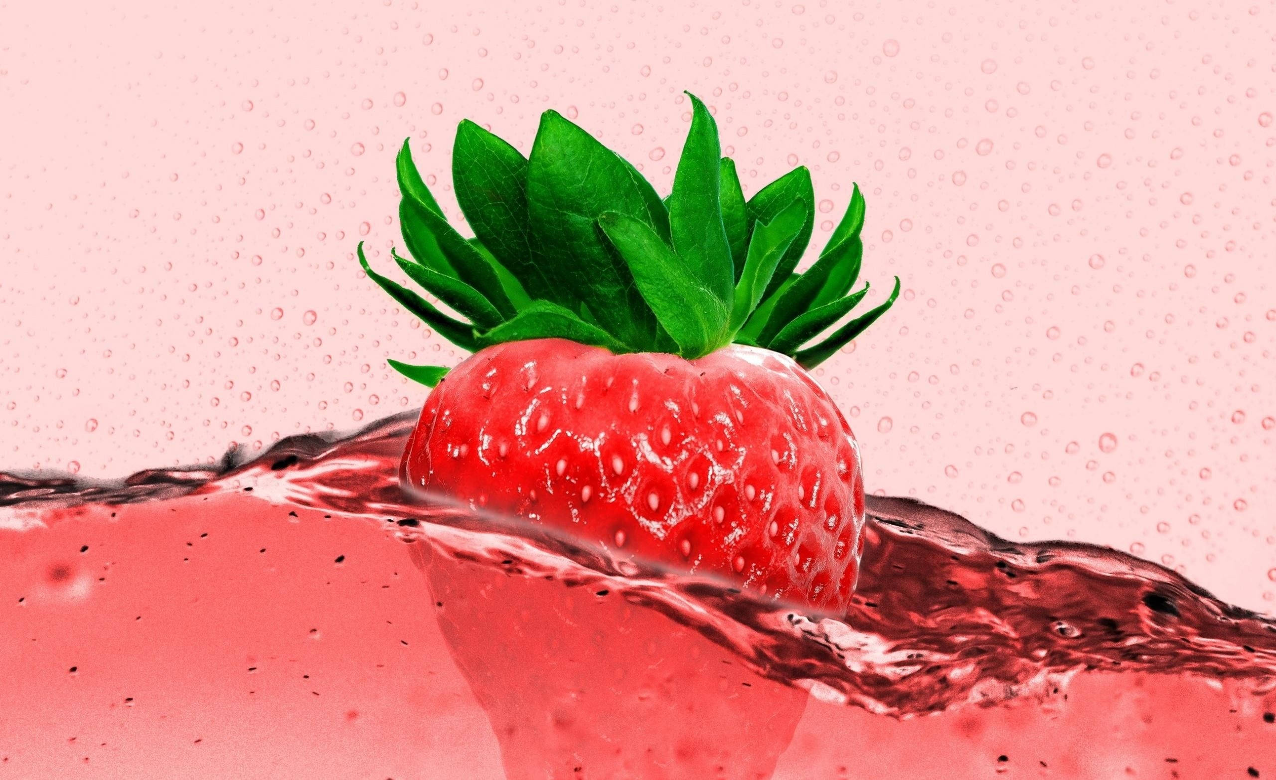 Strawberry Aesthetic 桌布 壁紙 — 一顆鮮紅色的草莓帶有綠色葉子，從粉紅色液體飛濺中浮現，背景是柔和的粉紅色。