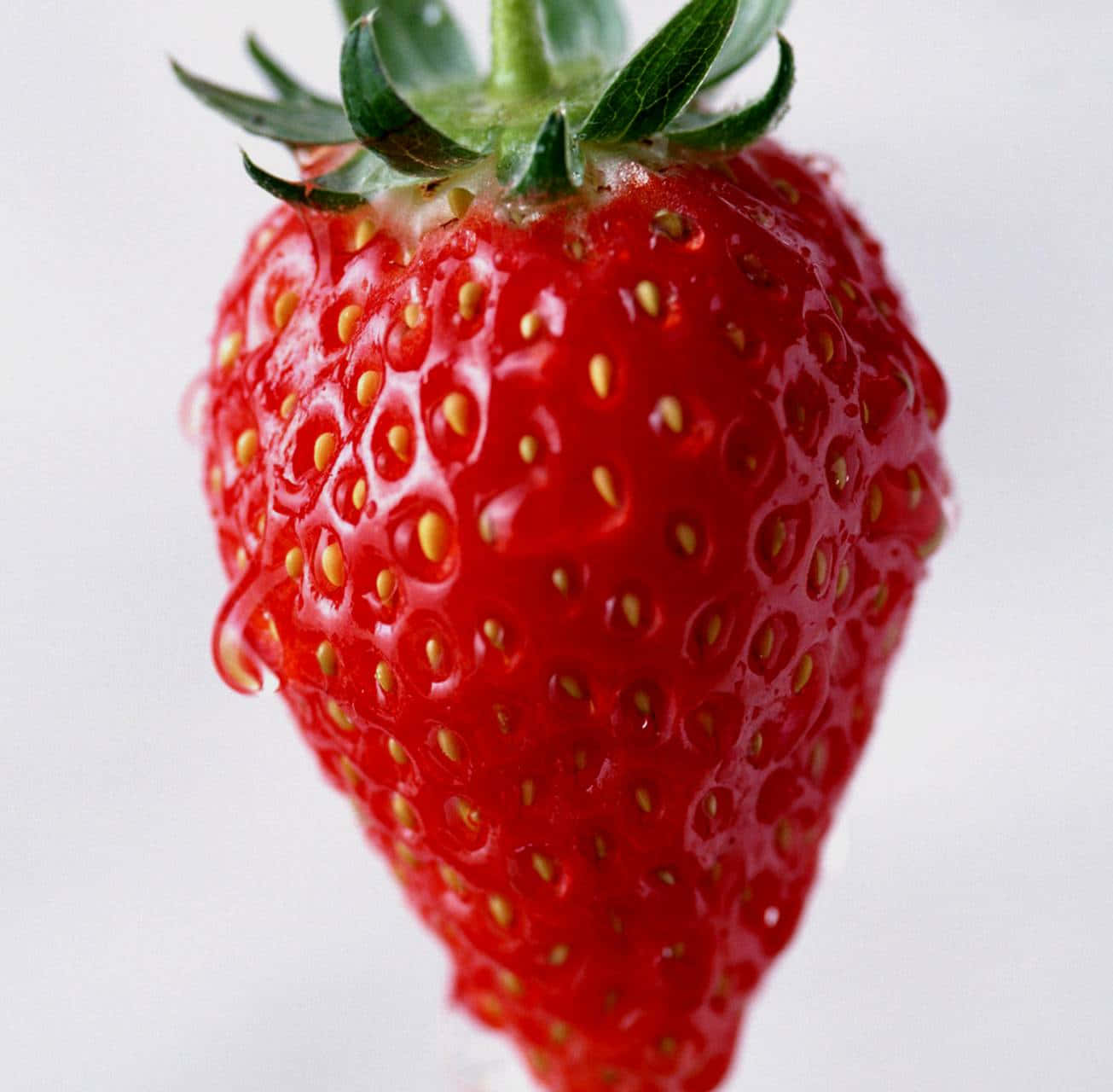 Red Strawberry 桌布 壁紙 — 一顆鮮紅色草莓的特寫，帶有綠色葉子和細小的黃色種子，閃爍著水滴。